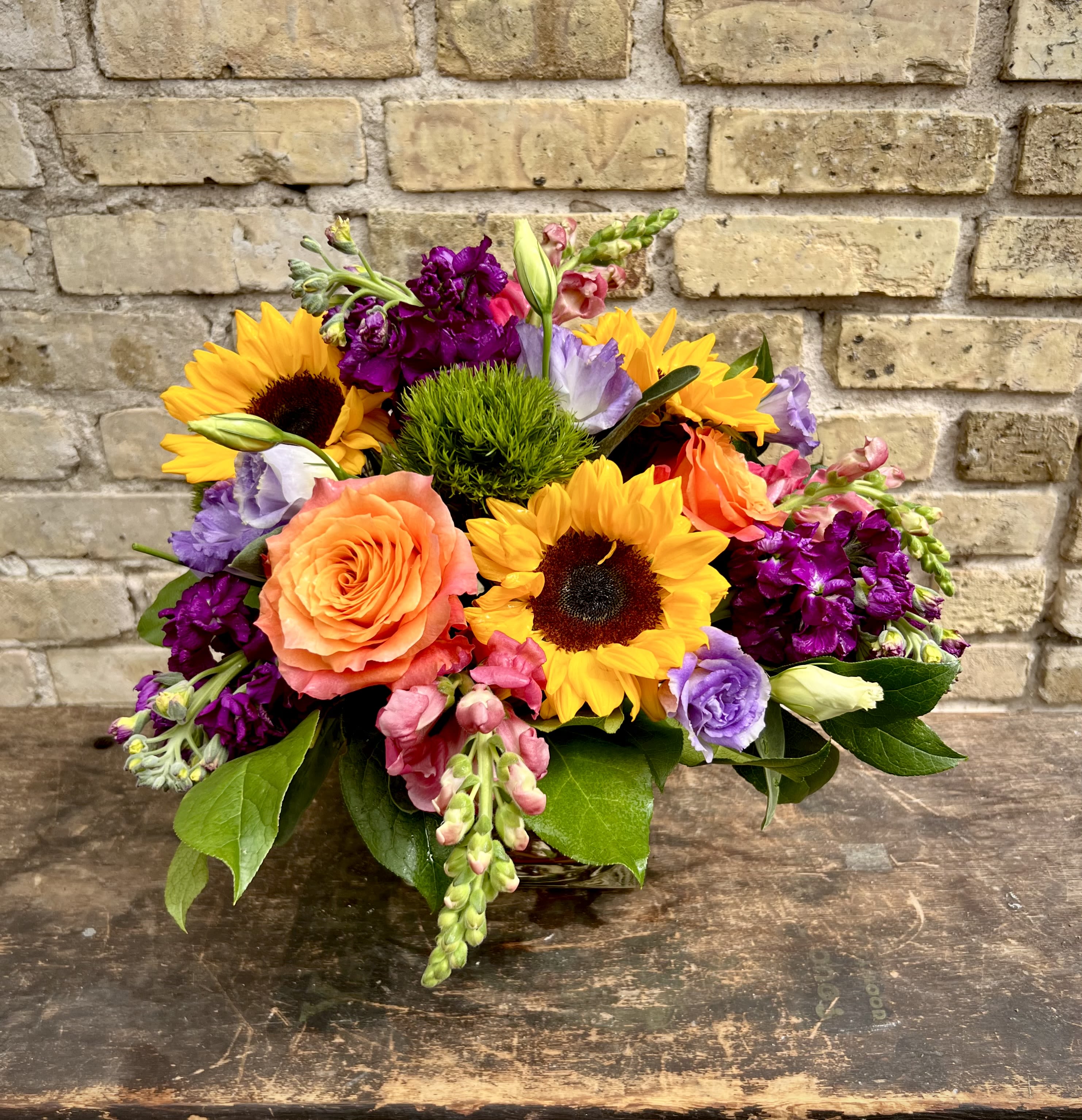 Mixed bouquet with sunflowers, roses, and purple blooms in a low arrangement
