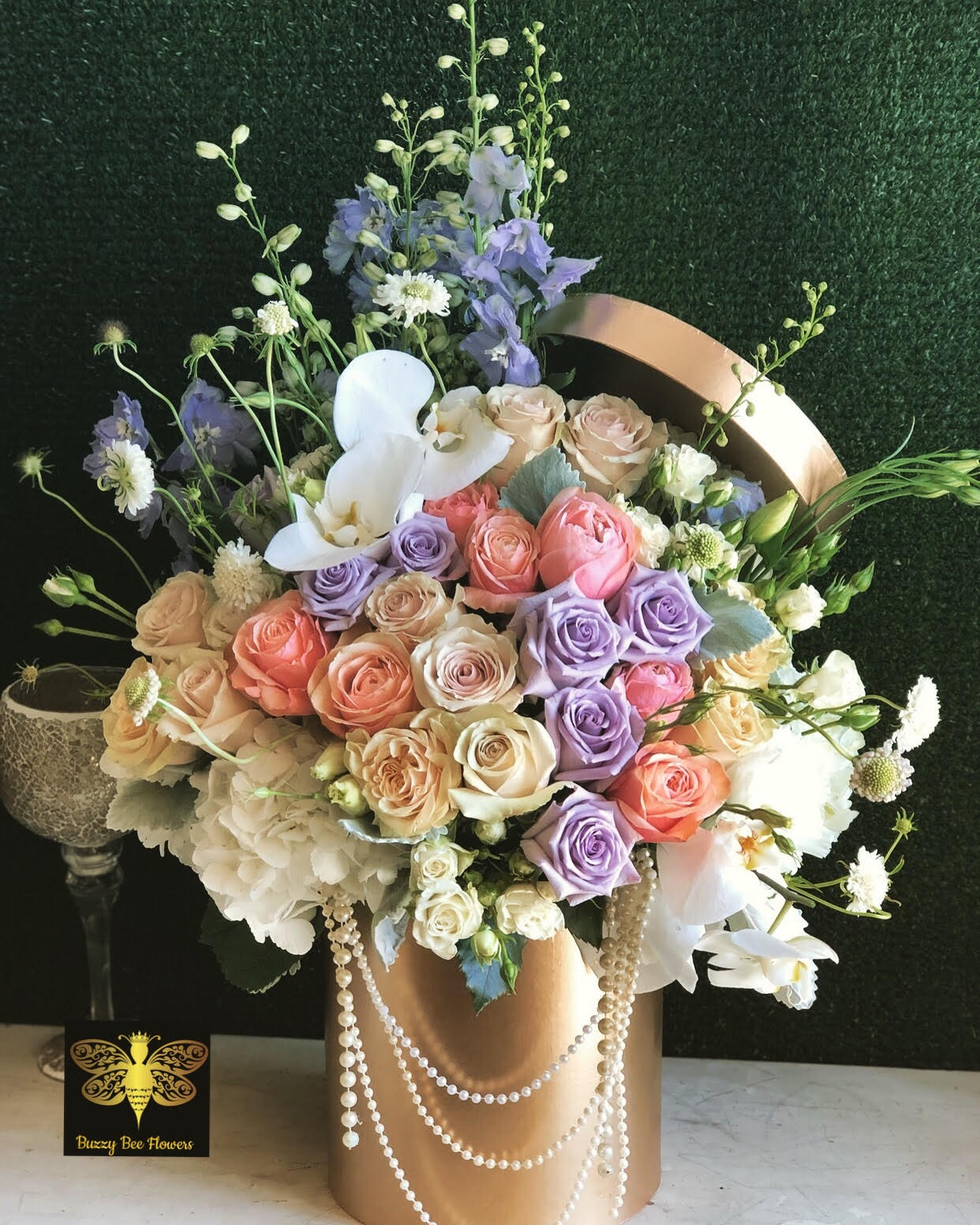 Pastel rose and orchid arrangement in a gold hatbox with pearl strands