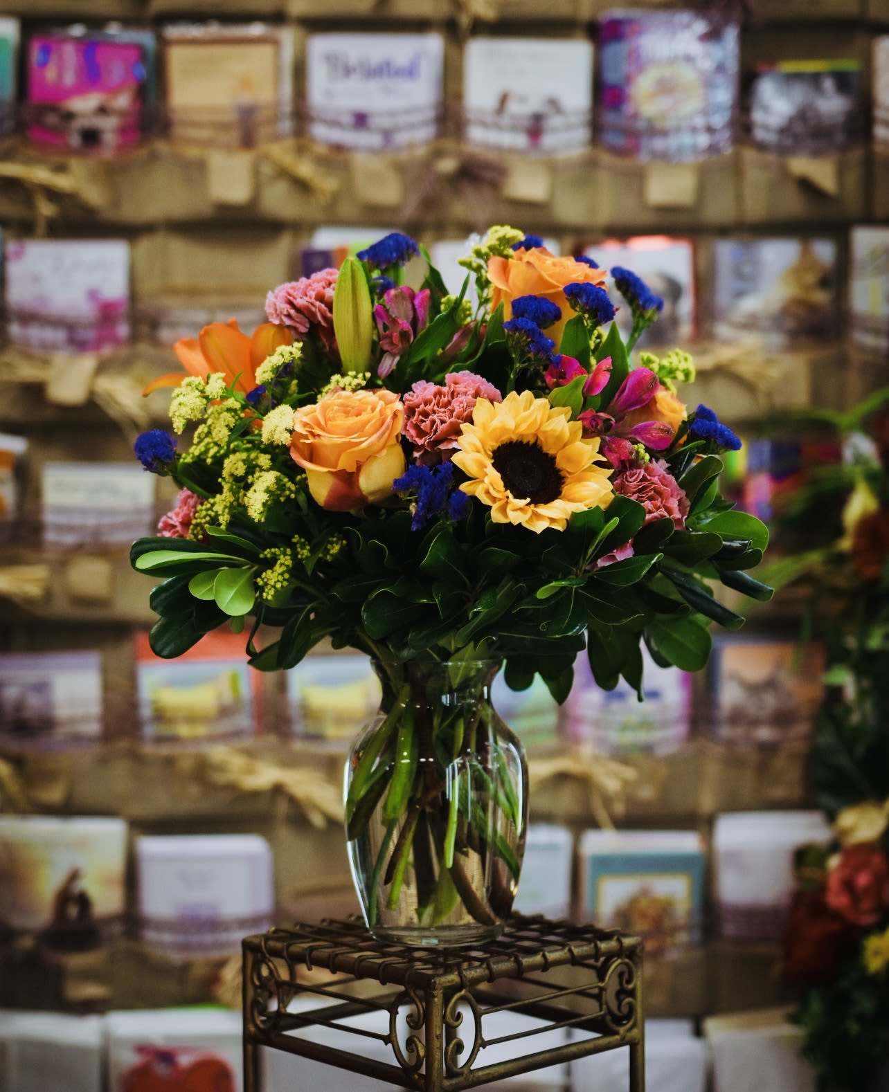 Mixed bouquet of orange, pink, yellow, and blue flowers in a glass vase
