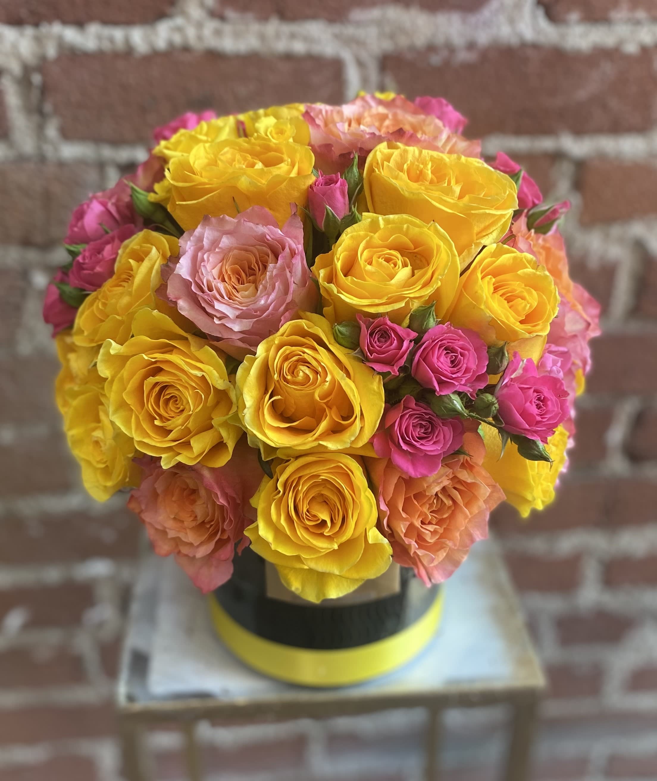 Bouquet of yellow, pink, and peach roses in a round box