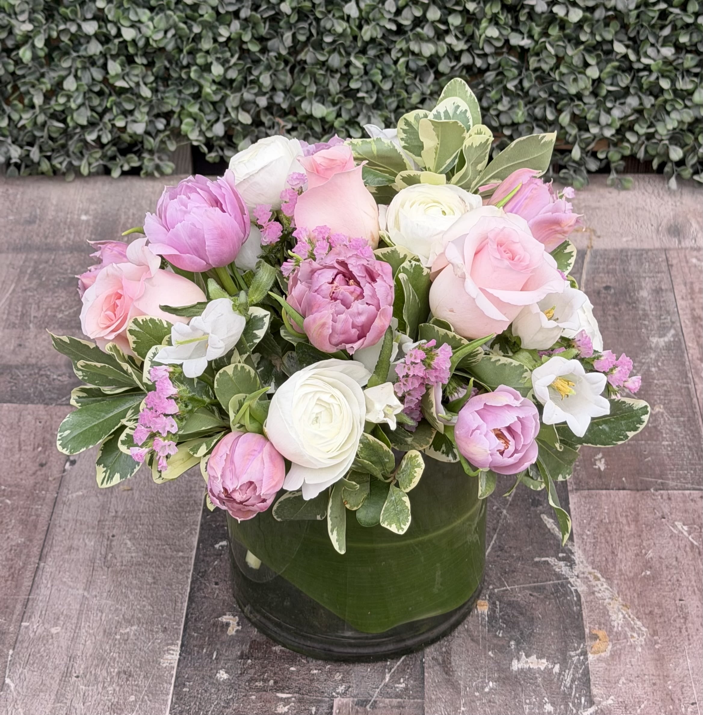 SERENITY - This pink and purple arrangement comes designed with roses, ranunculus, tulips, campanella and other flowers with assorted greens.  Designed in a glass vase. 