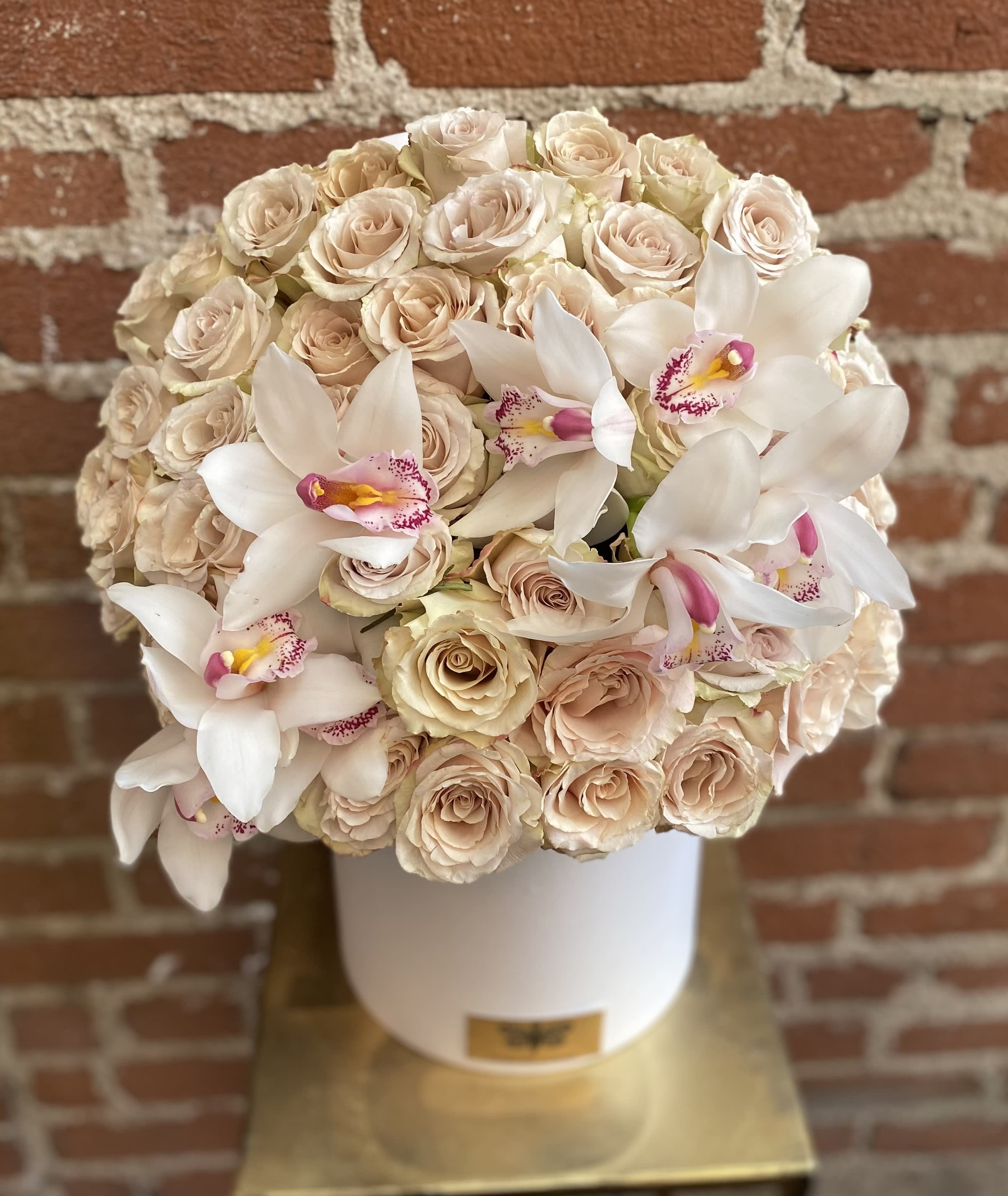 Cream roses and white orchids arranged in a white hat box