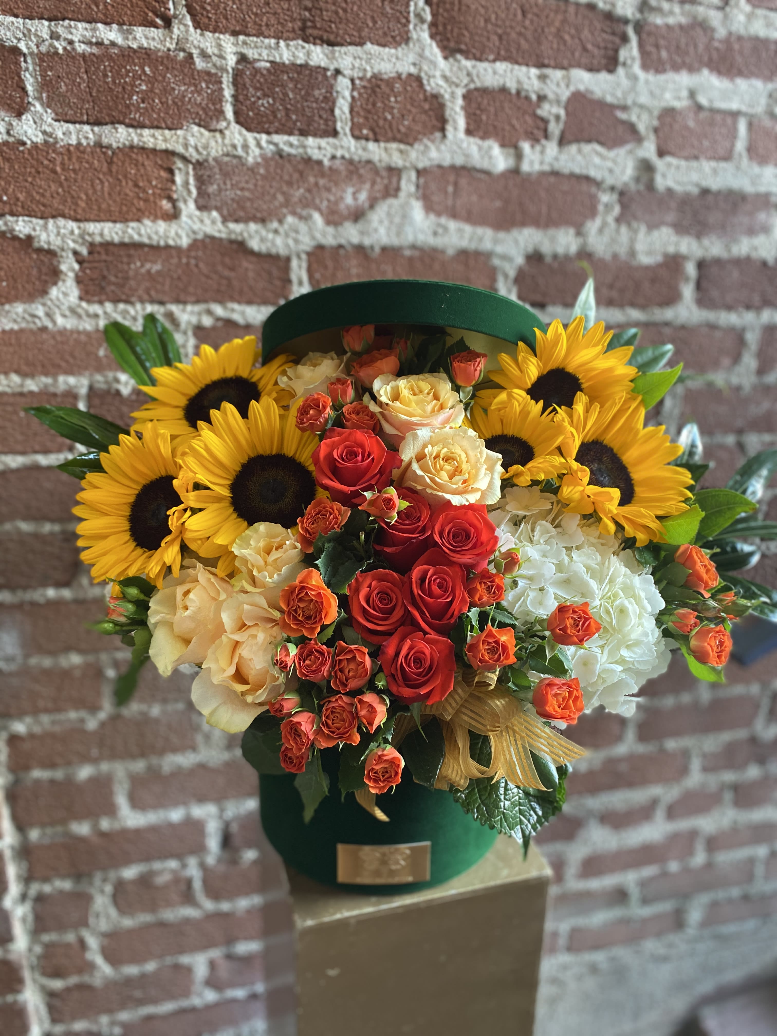 Bouquet of sunflowers, red and peach roses, and white hydrangeas in a green hatbox