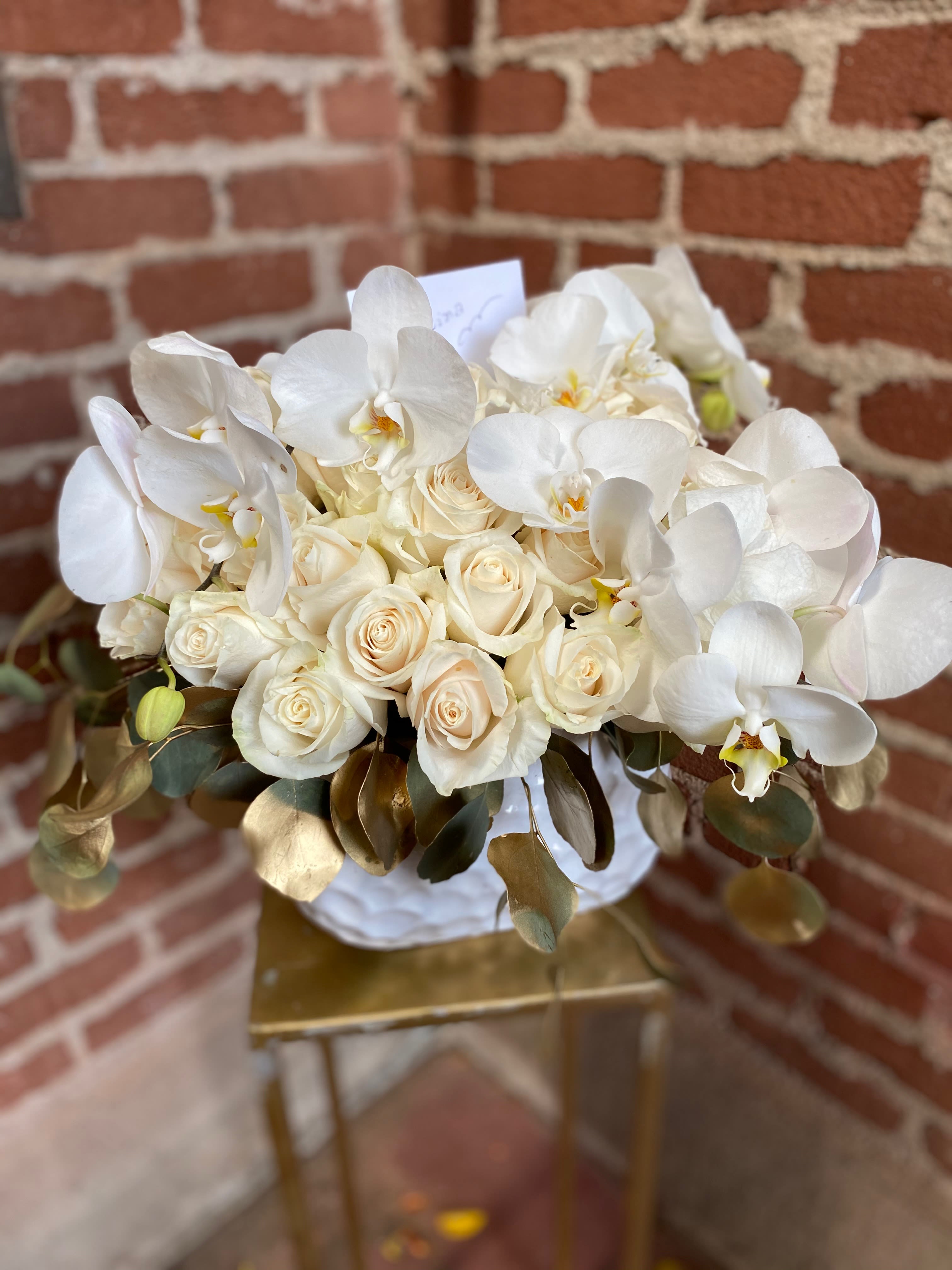 White roses and orchids in a round bouquet with gold-toned leaves