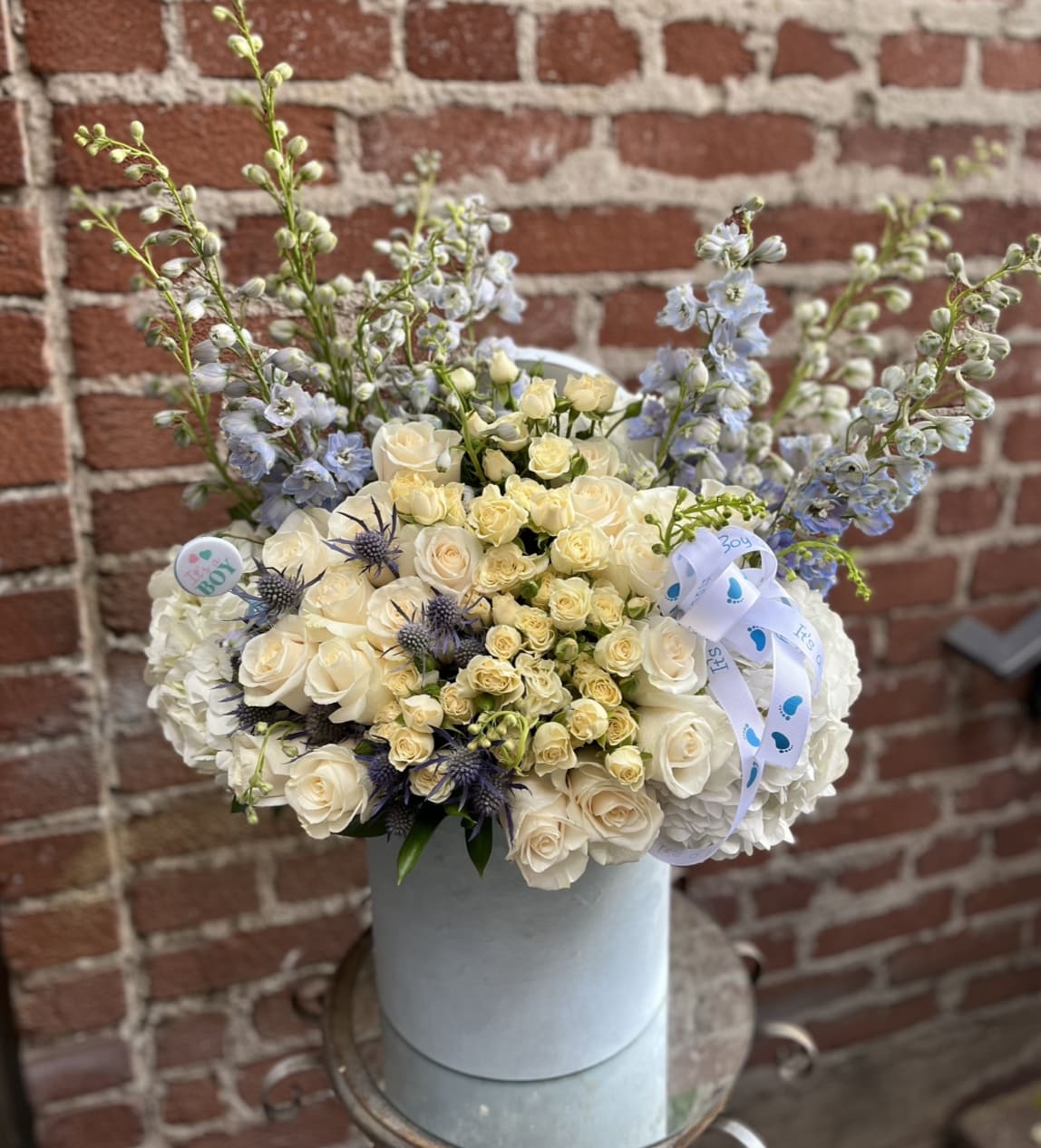 Cream roses and blue flowers arranged in a round hatbox