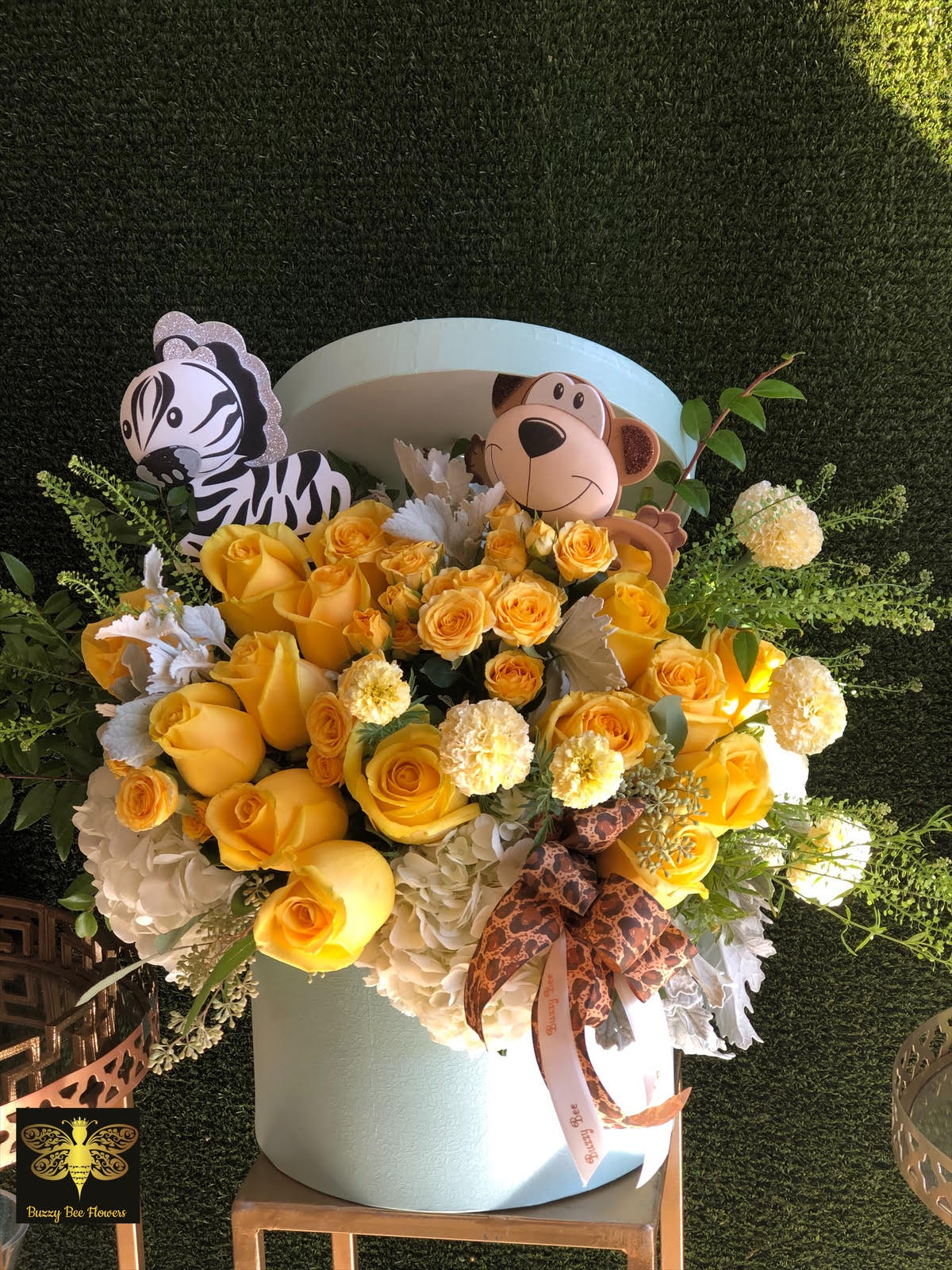 Yellow rose arrangement in a light blue hatbox with zebra and monkey toppers
