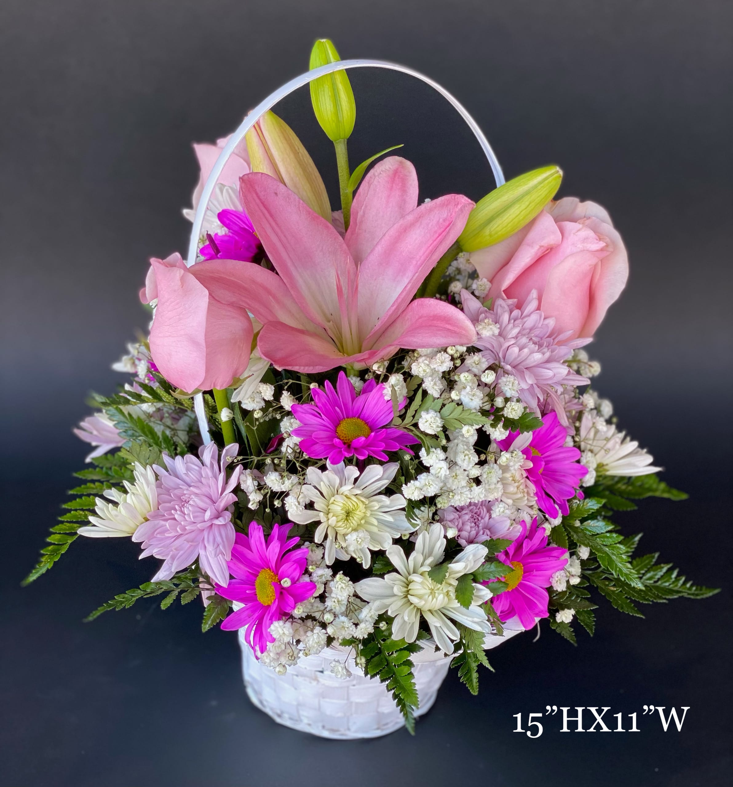 Pink lilies, roses, and daisies arranged in a white basket with a handle