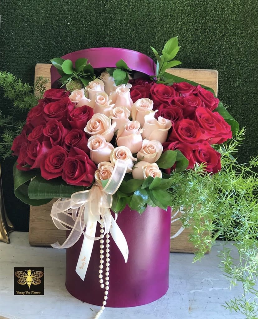 Round bouquet of red and blush roses in a magenta hatbox with ribbon