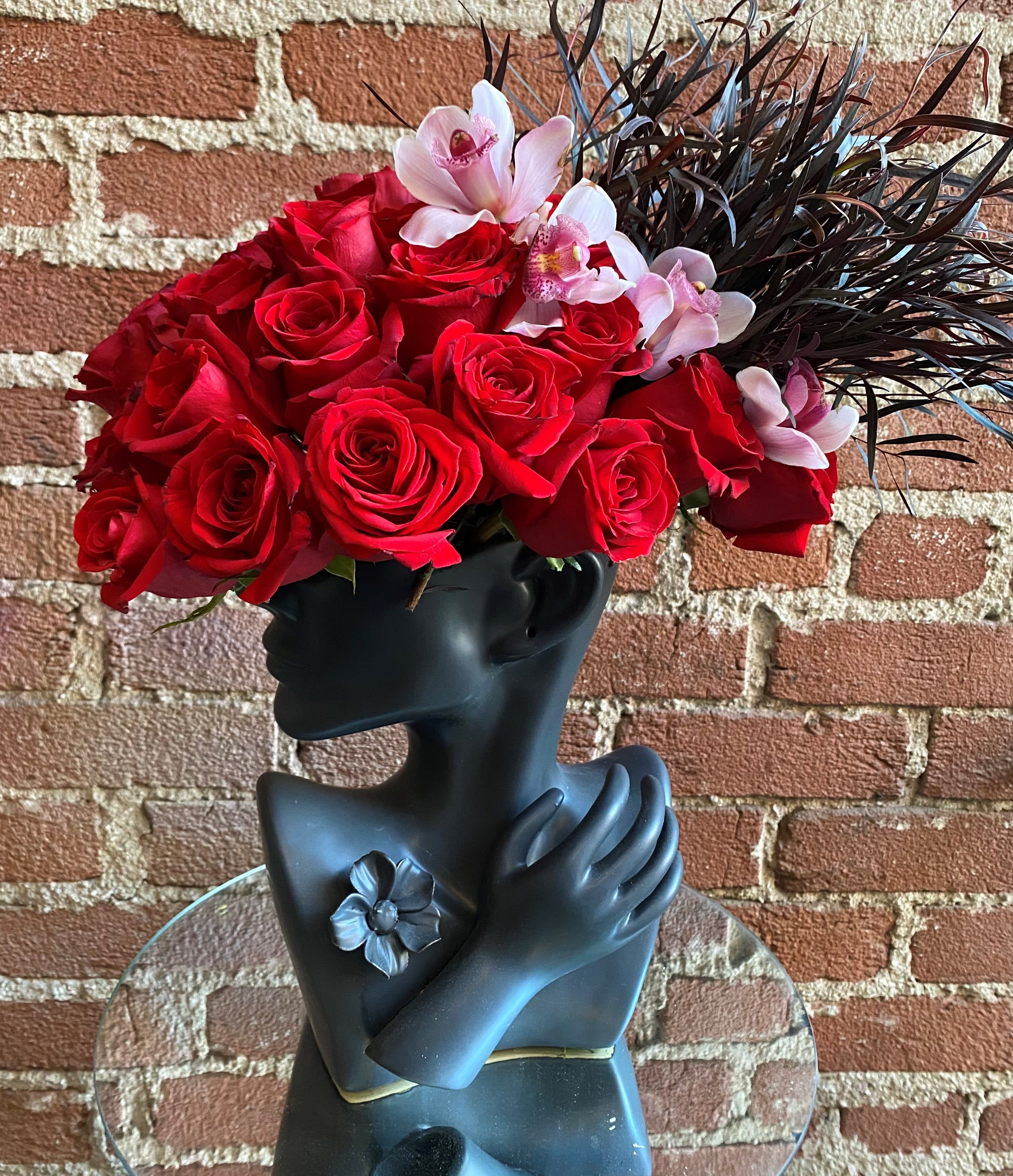 Red roses and pink orchids arranged in a black sculptural vase