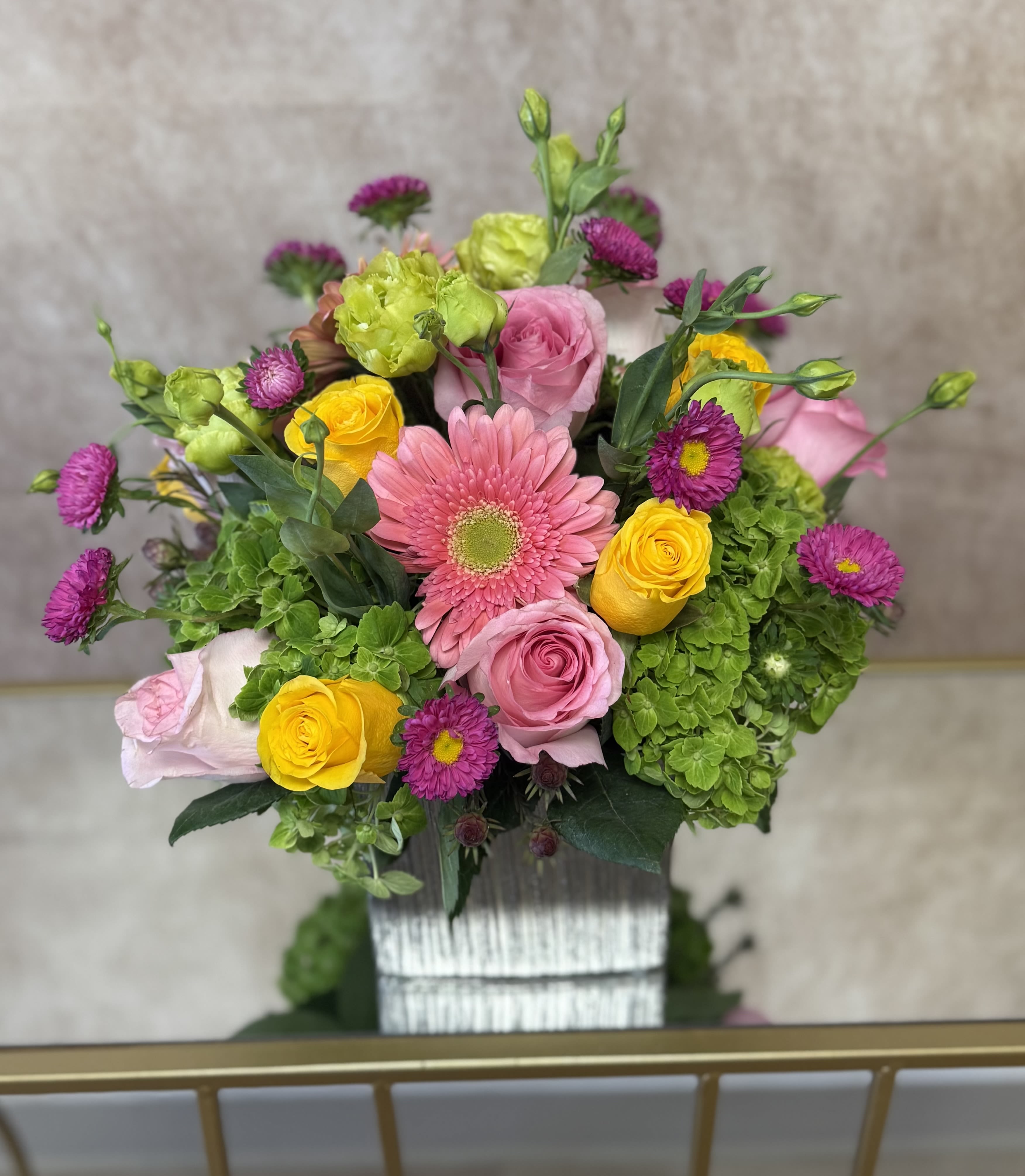 Mixed bouquet of pink, yellow, and purple flowers in a white container