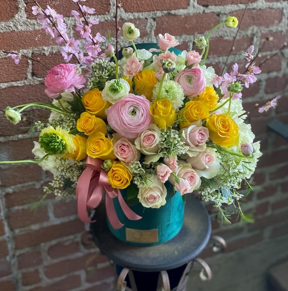 Bouquet of pink and yellow flowers in a teal hatbox with a pink ribbon