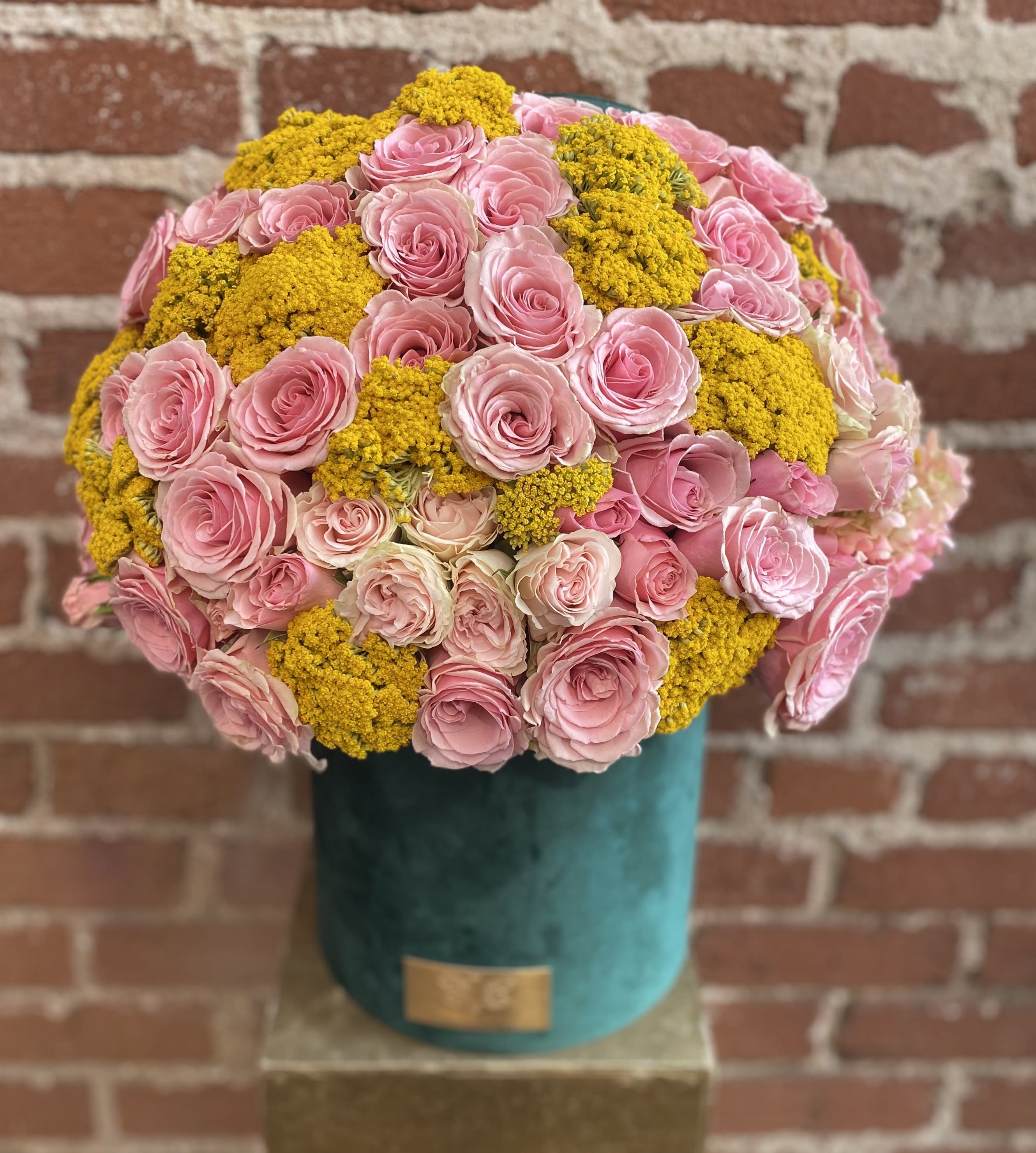 Pink roses and yellow clustered flowers arranged in a teal vase