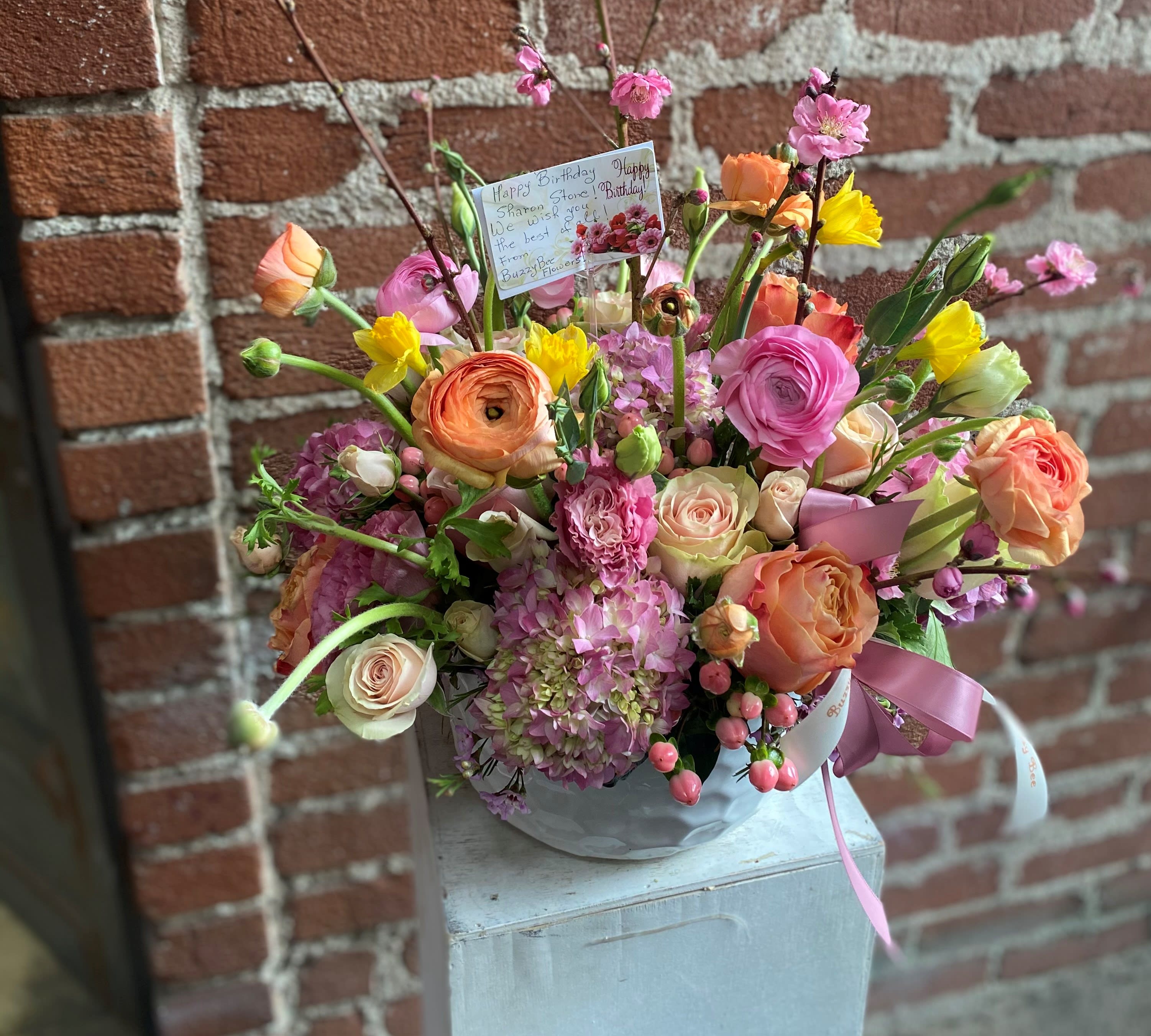 Mixed bouquet of pink, peach, and yellow flowers in a round container