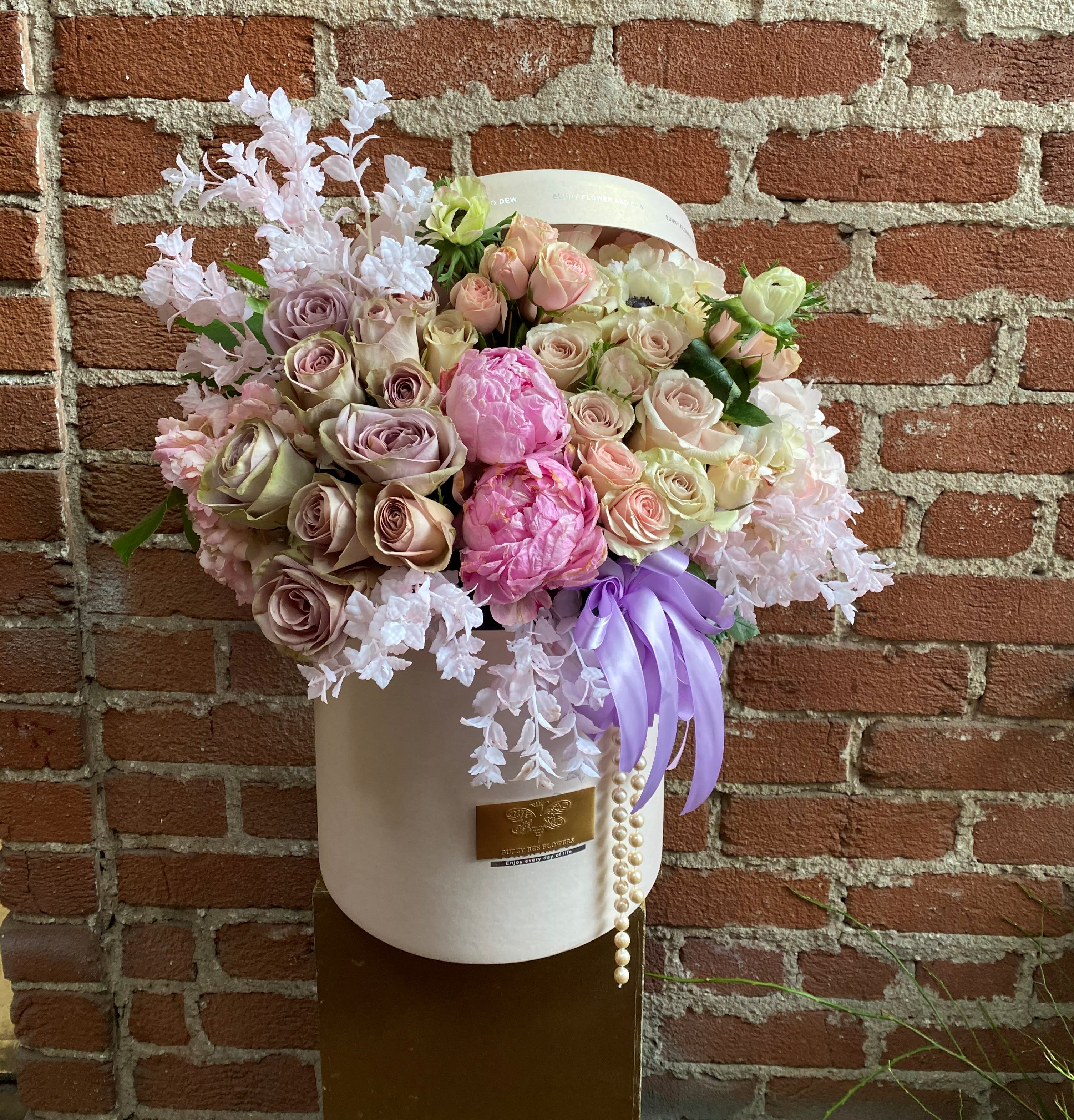 Pastel bouquet of roses and peonies in a white hatbox with a lavender ribbon