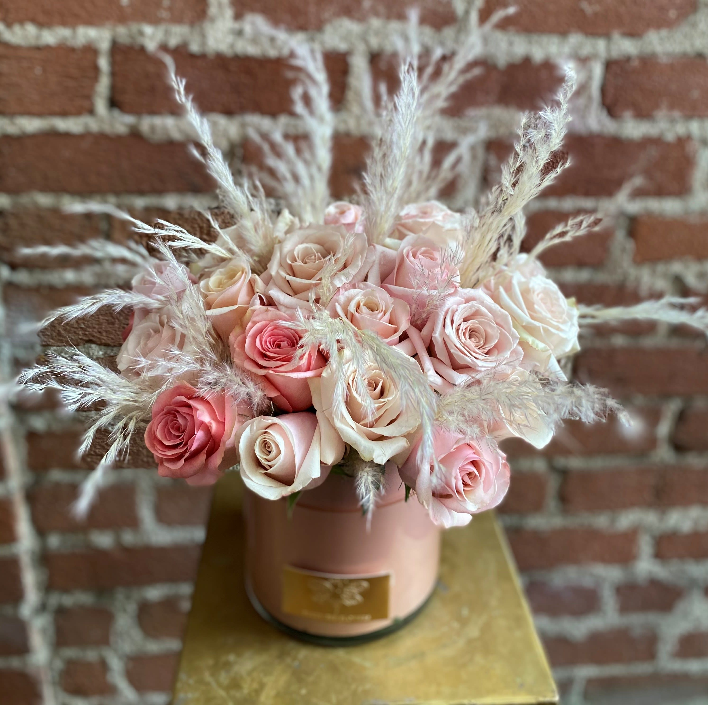 Pink and blush roses arranged in a round box with feathery accents