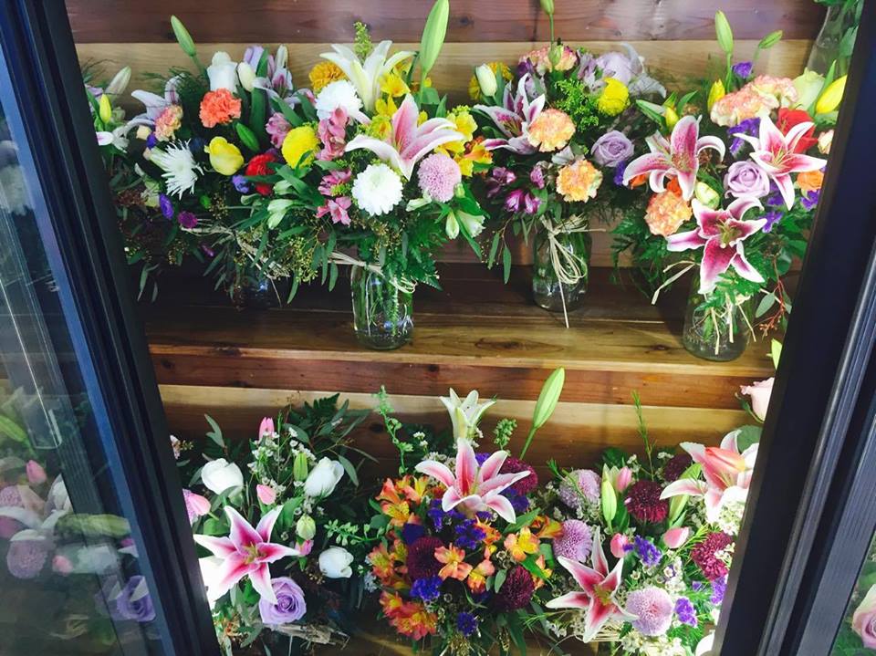 Assorted colorful flower bouquets arranged on wooden shelves in glass jars