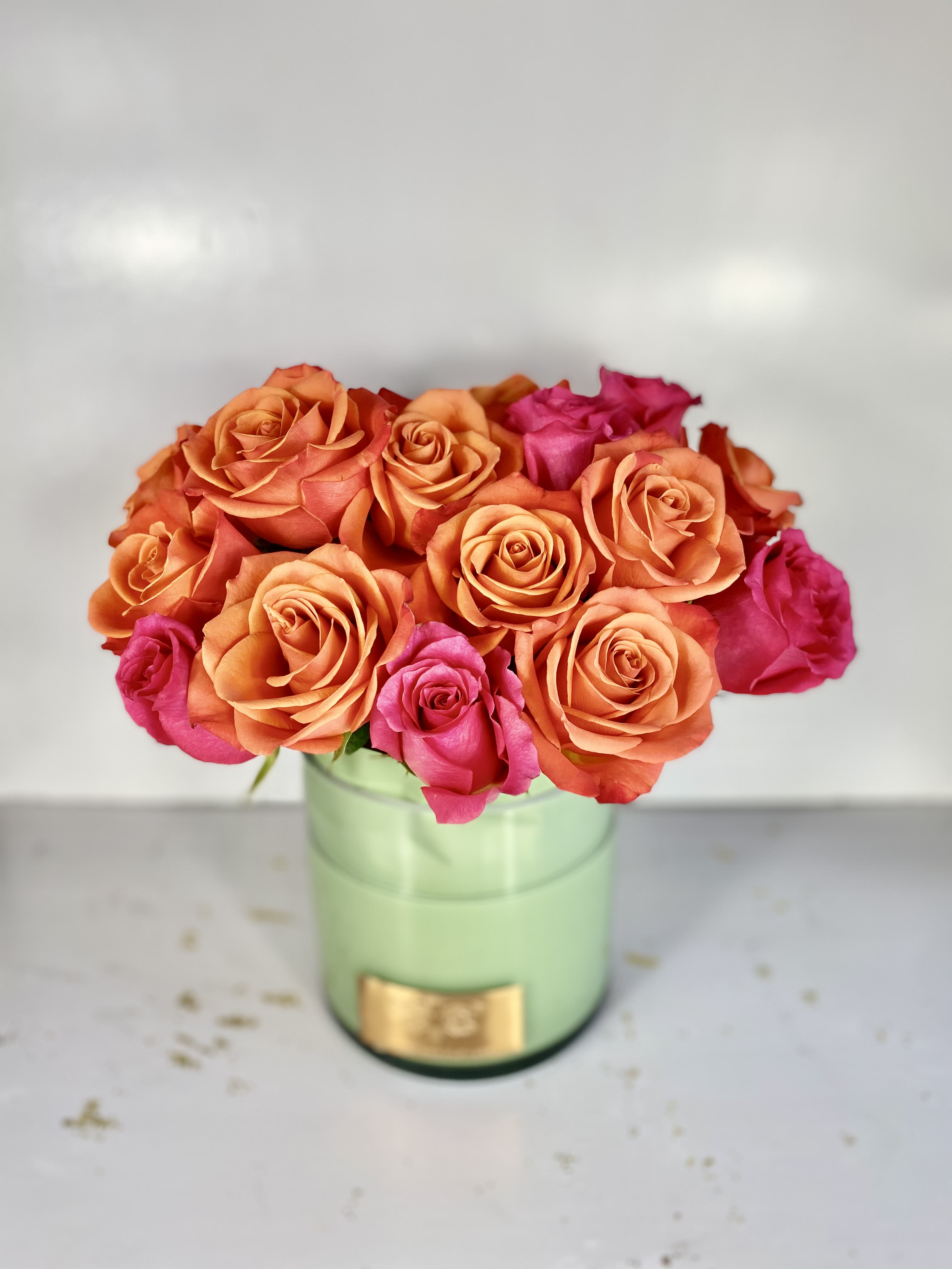 Orange and pink roses arranged in a green round box