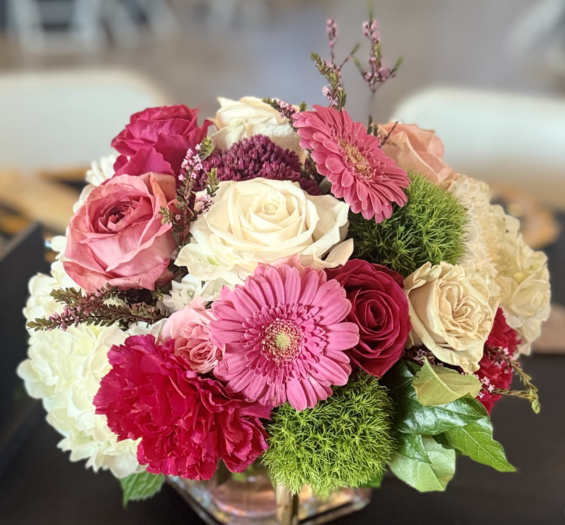 Round arrangement of pink gerbera, roses, carnations, and cream blooms in a glass cube vase