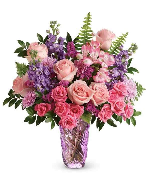 Cherry Blossoms - Pale pink roses and bright pink spray roses mingle with purple stock and pink-and-white alstroemeria in a lush, rounded bouquet-an airy Cherry Blossoms flower arrangement that reads romantic and celebratory. Perfect as a birthday bouquet, anniversary flowers, or a thoughtful just-because gift, this design gives the person you're thinking of an immediate sense of warmth and delight with its soft blush tones punctuated by vivid purple accents.  Arranged in a clear purple glass vase, the mix of roses, stock, alstroemeria, and chrysanthemums creates a full, textured silhouette with fresh greenery for contrast. The vase's reflective finish reinforces the coordinated palette while keeping the overall look modern and bright. Sized for everyday display, it arrives ready to set on a table or mantel and feels like the kind of bouquet that will lift spirits and make someone feel truly seen.