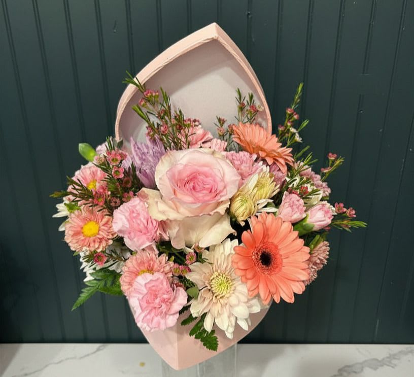 The Blooming Heart - A blush pink hatbox filled with soft pink roses, pale lilies, and cheerful daisy-like blooms creates an immediately romantic birthday bouquet or Mother's Day gift that reads as gentle and thoughtful. The pastel mix of pink, white, peach, lavender and touches of pale yellow gives the arrangement a garden-fresh look. Available in a small or large gift-ready hatbox, the presentation is polished and feminine.