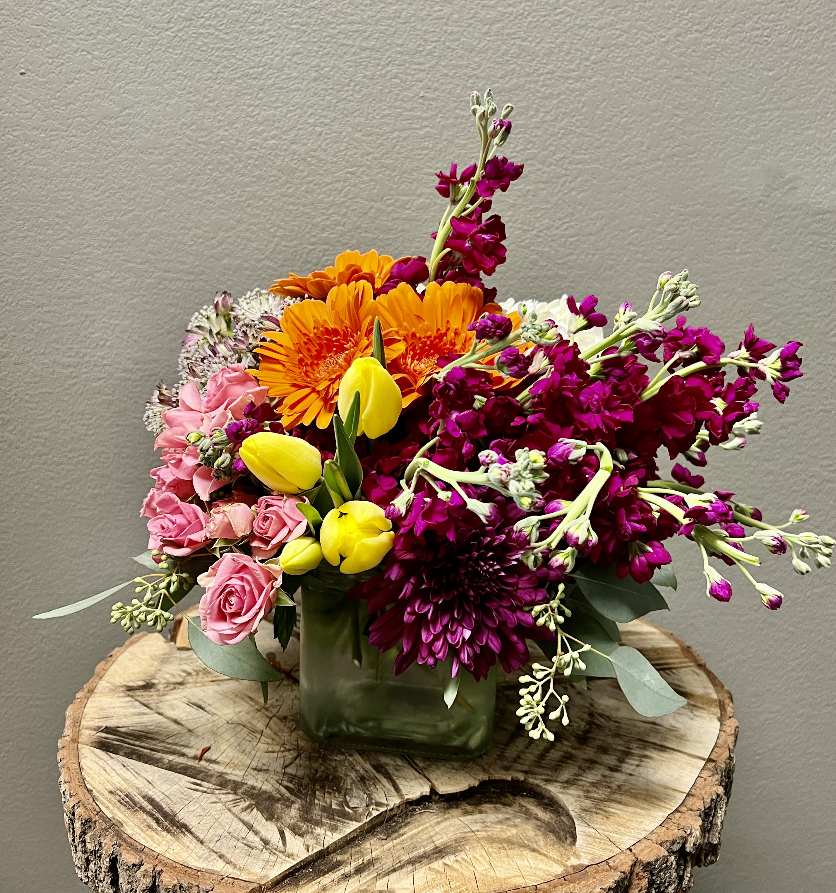 Mixed bouquet in a square glass vase with pink, orange, yellow, and magenta flowers