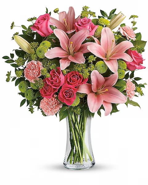 Dressed To Impress - Large pink lilies and bright pink roses create an immediate wow-this flower arrangement is a romantic birthday bouquet or anniversary gift that reads as both elegant and exuberant. The pink, green, and white palette is vivid yet soft: lush magenta roses pop against pale blush carnations, while green button-like filler blooms and dark foliage add depth so the person you're thinking of will feel truly noticed.  Arranged in a clear glass vase, the design is full and rounded with layered textures from the lilies' broad petals to the rosebuds and ruffled carnations. The upright presentation measures as a classic tabletop size that works equally well on a dining table, office desk, or bedside stand. It's an ideal springtime pick-me-up or everyday celebration piece that sends a message of warmth and admiration.  This bouquet suits birthdays, anniversaries, and simple "thinking of you" moments-perfect for the recipient who appreciates a fresh, romantic look. Water daily and keep away from direct heat to preserve blooms; available to order in standard sizing for same-week delivery.