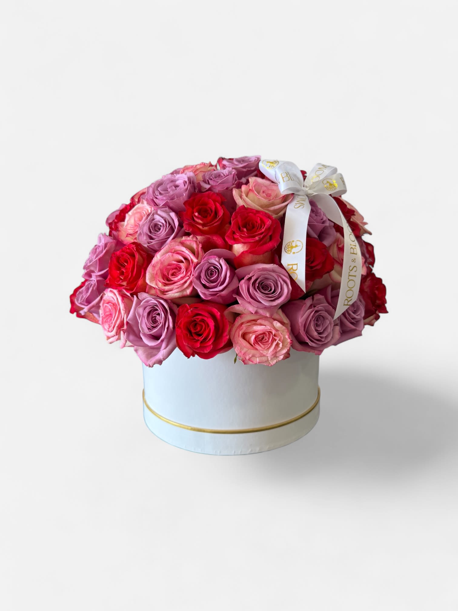 Round box arrangement of pink, lavender, and red roses with a ribbon bow