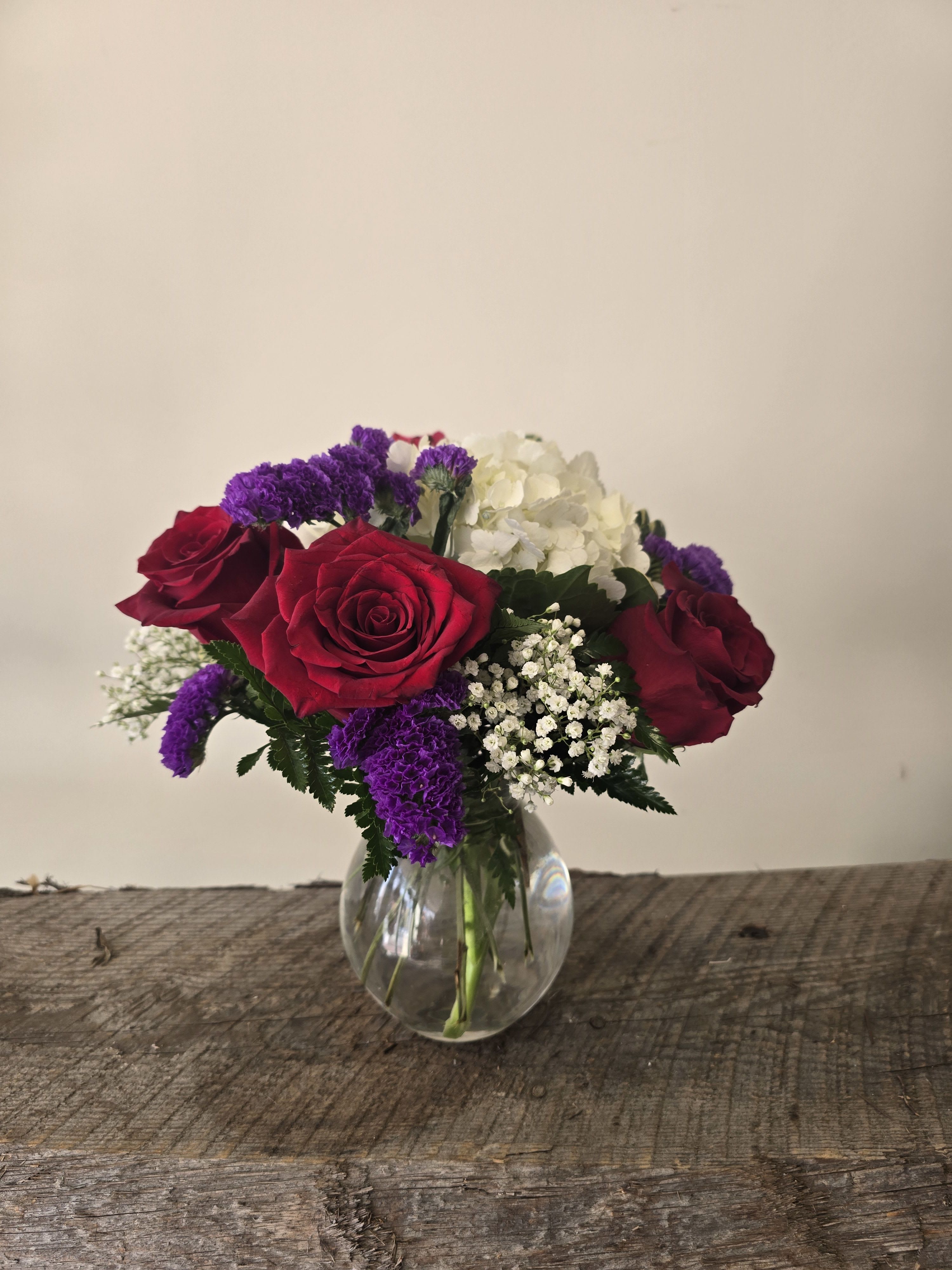 Bouquet of red roses, white hydrangea, and purple filler in a clear glass vase