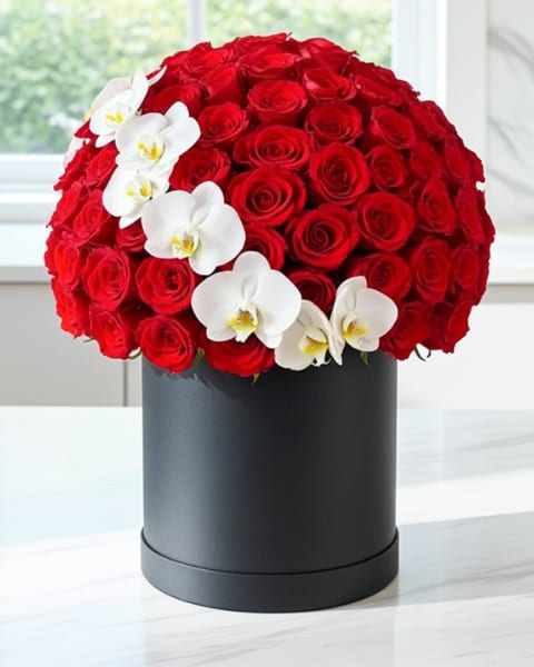 Fresh Red Roses Box - A dense dome of vivid red roses meets a diagonal spray of white Phalaenopsis orchids in this romantic flower arrangement-perfect as a red roses box for anniversaries, Valentine's Day, or a heartfelt birthday gift. The striking red-and-white contrast creates a polished, formal look that reads as both passionate and elegant, the kind of present that makes the person you're thinking of feel deeply celebrated.  Arranged in a matte black cylindrical hatbox, the bouquet's saturated crimson roses feel especially full and luxurious against the clean white orchids and the sleek black container. The compact, rounded silhouette is modern and giftable; colors are red, white, and black with roses and Phalaenopsis orchids as focal blooms. The hatbox presentation makes it easy to display on a table or bedside and keeps the design looking neat and intentional.  This arrangement suits romantic occasions, milestone anniversaries, and refined birthday gestures-or as an everyday way to make someone feel truly seen. Order with confidence for same-week gifting; the hatbox keeps stems neatly contained and the flowers looking fresh while you arrange delivery or presentation.
