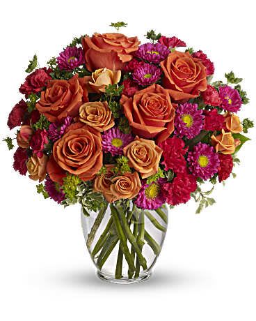 Orange roses and magenta daisies in a clear glass vase