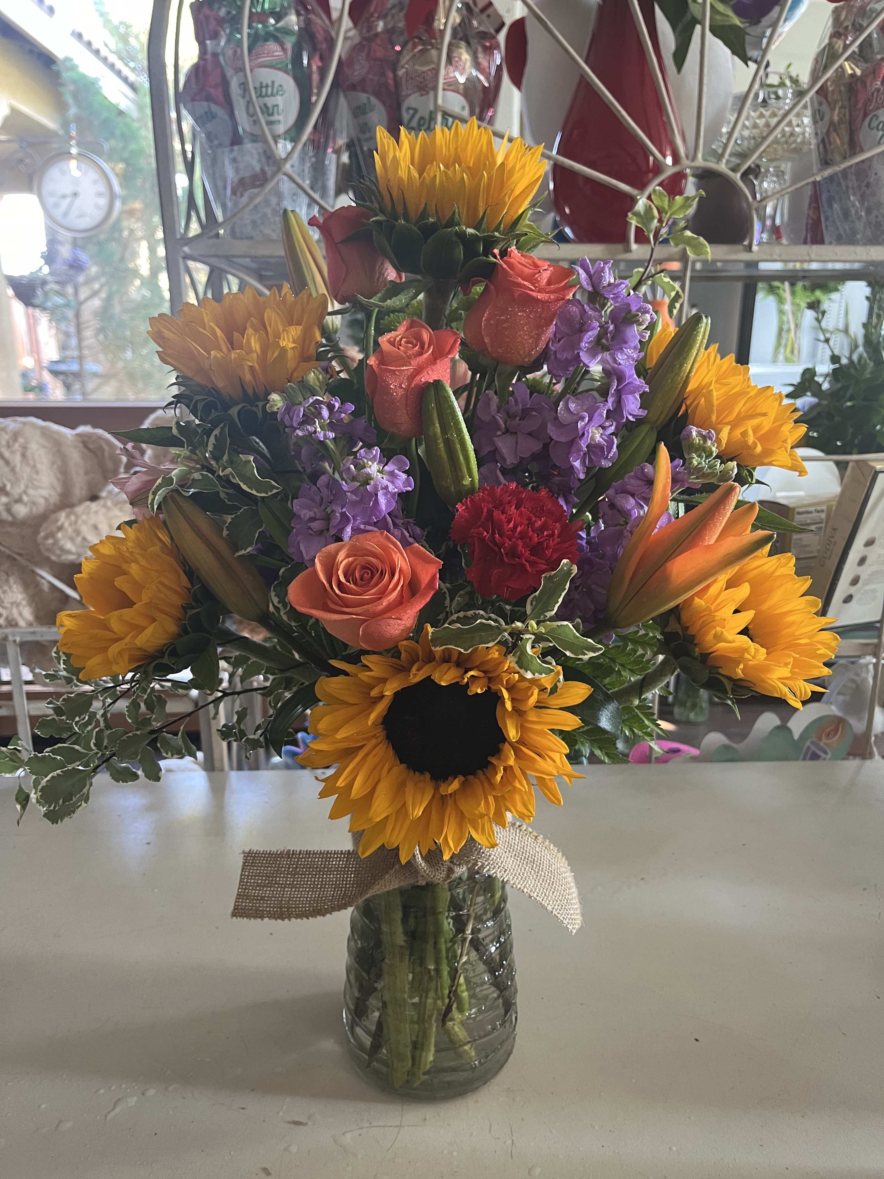 Mixed bouquet with sunflowers, roses, lilies, and purple blooms in a glass vase
