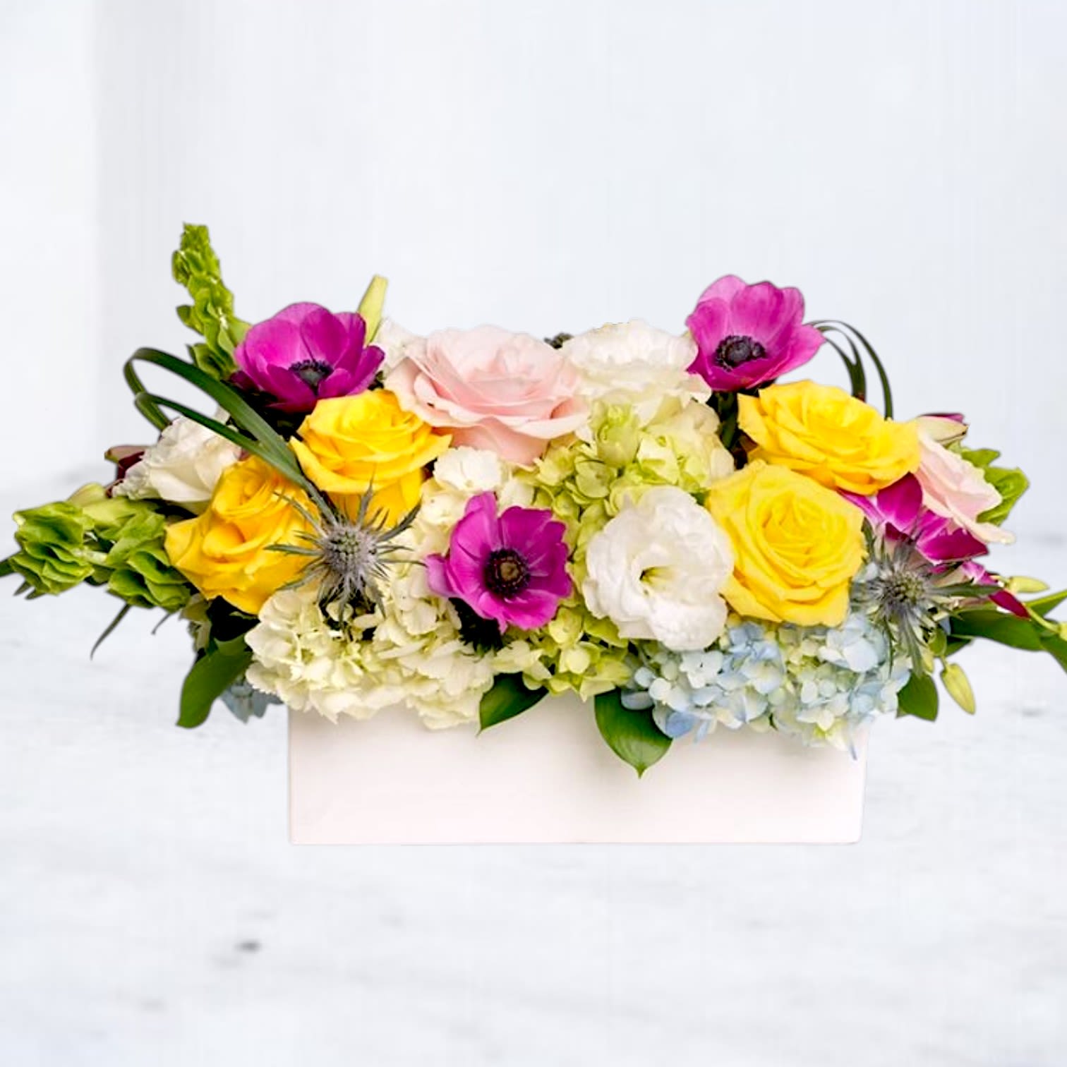 Pop Rocks - Pop Rocks is a vibrant modern flower arrangement designed with bright yellow roses, pink anemones, hydrangea, lisianthus, orchids, and seasonal blooms in a sleek rectangular vase. Bursting with playful color, layered texture, and contemporary garden-inspired styling, this arrangement blends bold pinks, sunny yellows, crisp whites, and soft blue accents for a fresh editorial look.  Perfect for birthdays, celebrations, thank you flowers, congratulations gifts, luxury everyday flowers, and statement floral delivery, Pop Rocks brings together cheerful seasonal blooms with elevated modern design for an arrangement that feels energetic, artistic, and unforgettable.  Handcrafted with premium seasonal flowers and available for same-day flower delivery in Magnolia, TX and surrounding areas including The Woodlands, Montgomery, Conroe, Spring, Tomball, and Lake Conroe communities.