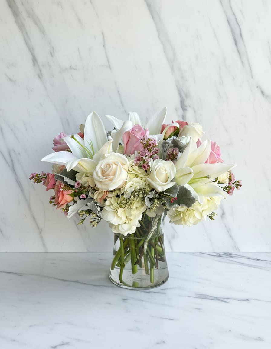 Pink and white bouquet with lilies and roses in a clear glass vase
