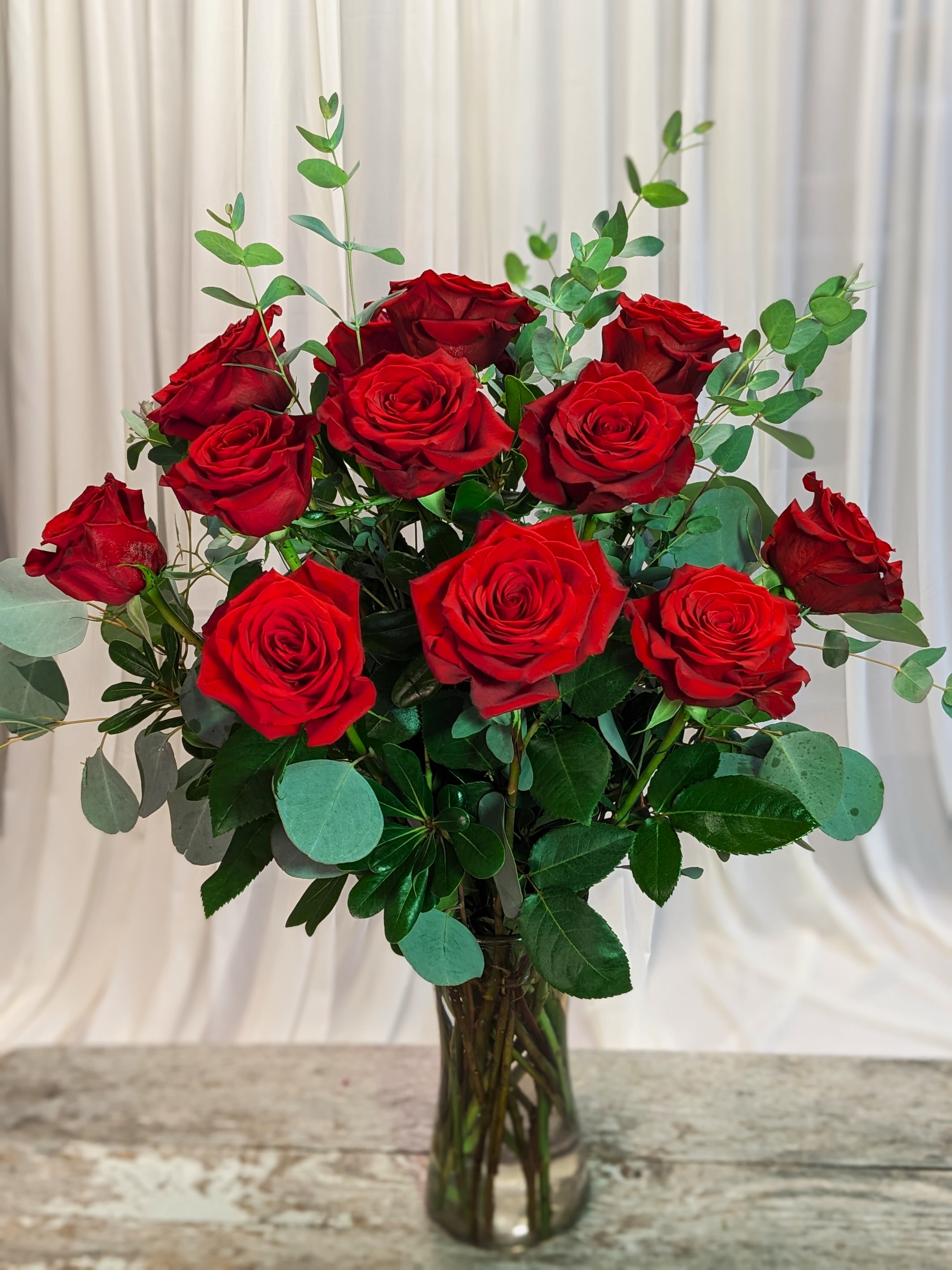 Red roses arranged in a clear glass vase with eucalyptus