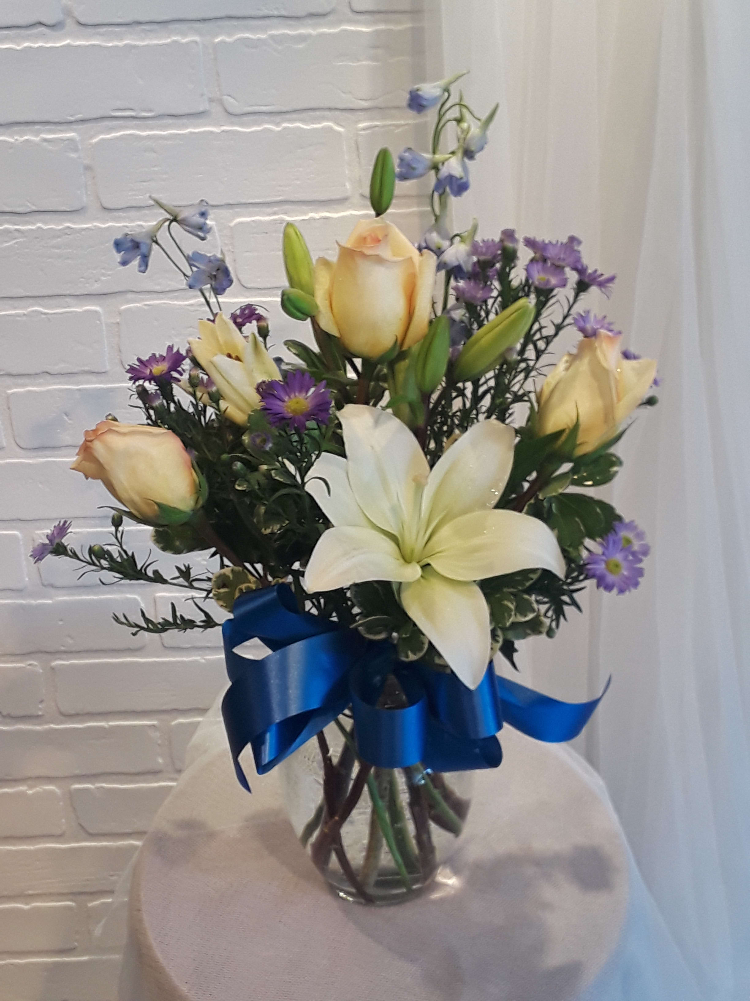 Bouquet of white lilies, cream roses, and purple flowers in a glass vase