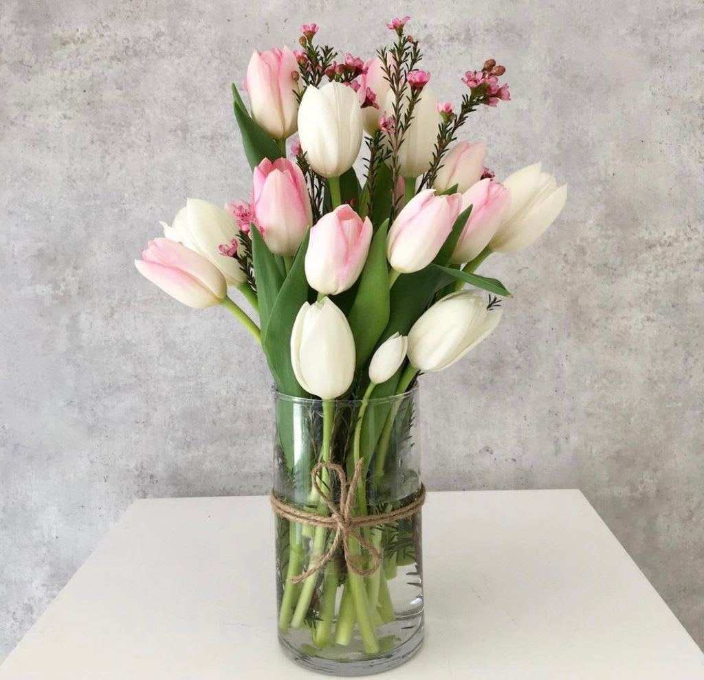 Pink and white tulips in a clear glass vase tied with twine