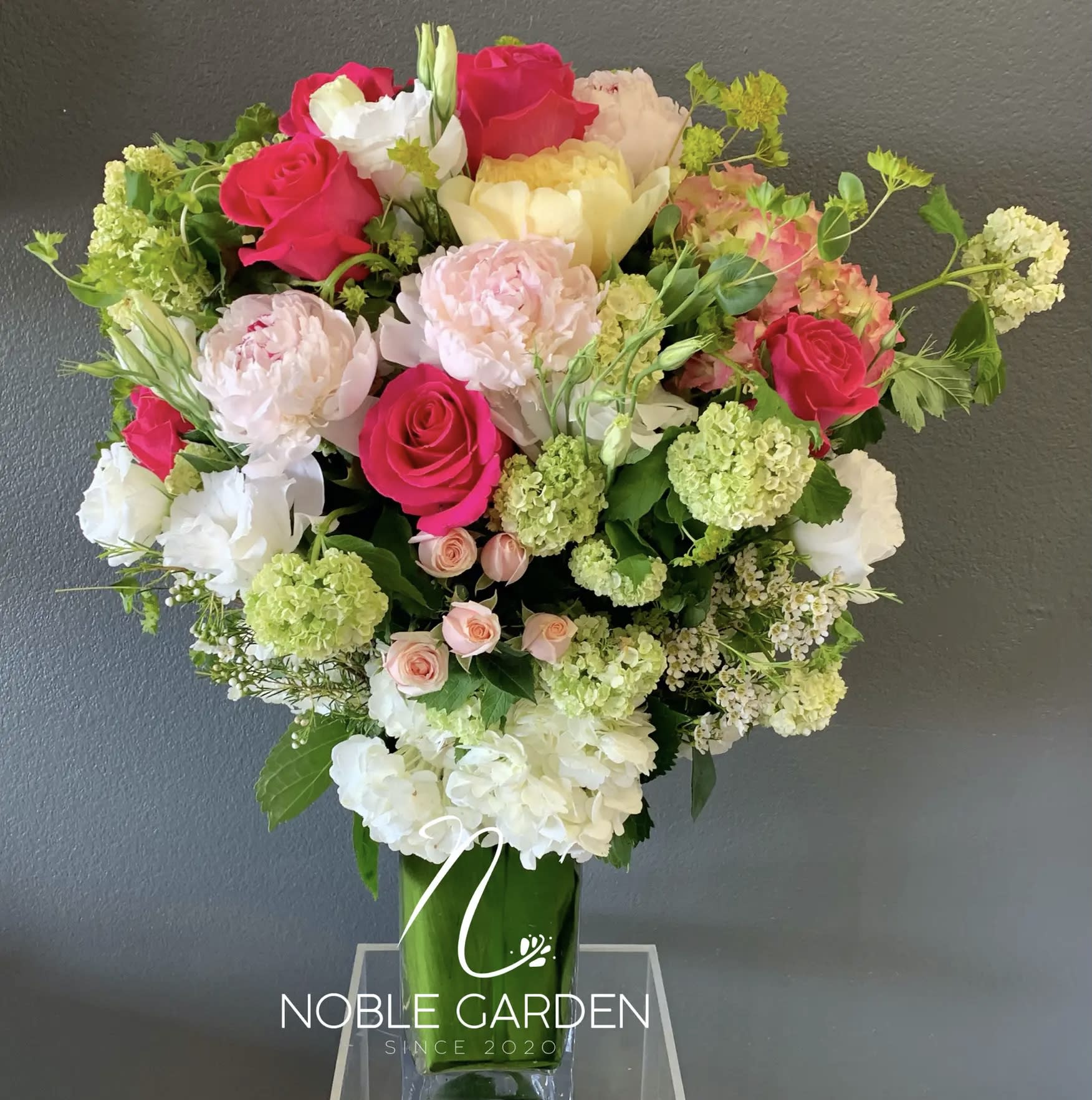 Mixed bouquet of pink, white, and green flowers in a tall glass vase