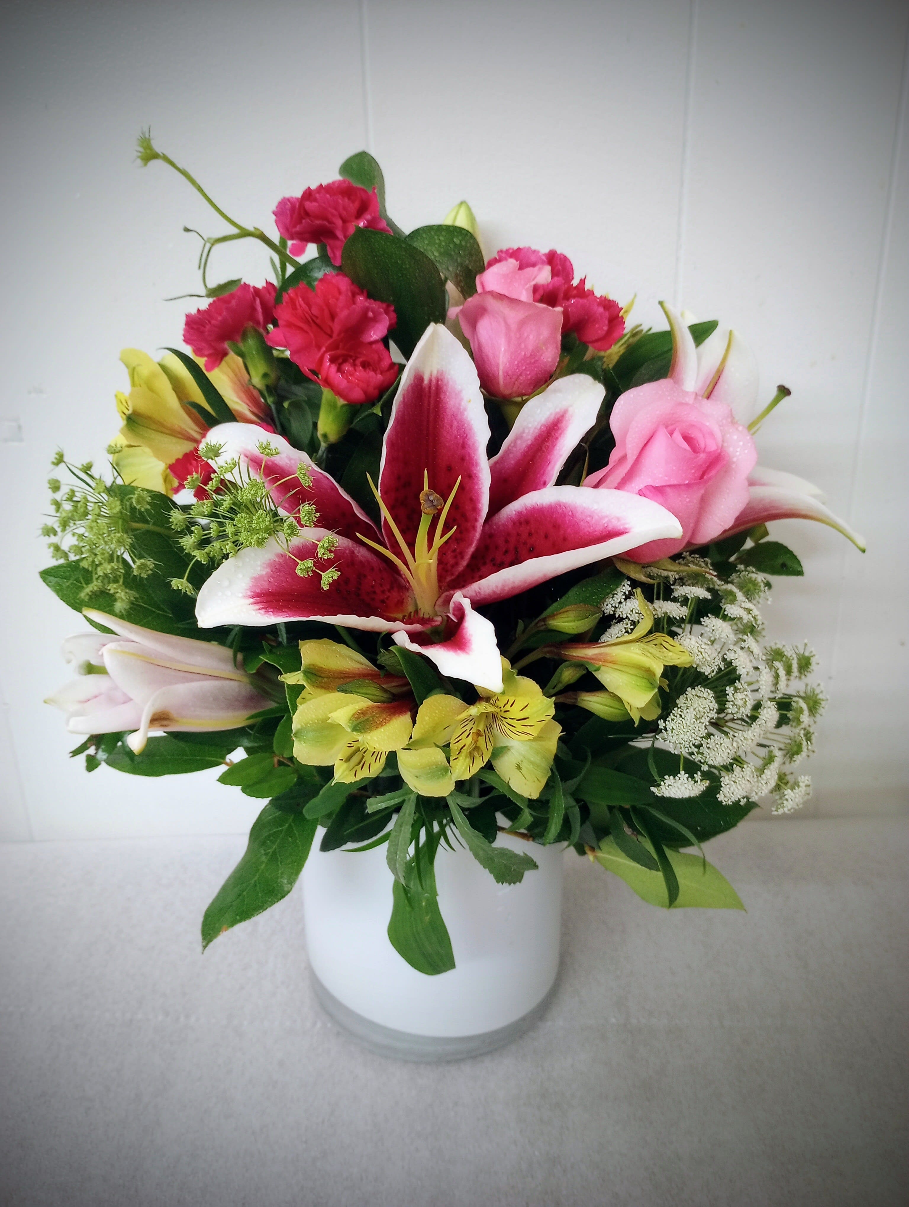 Mixed bouquet of pink roses, lilies, and carnations in a white vase