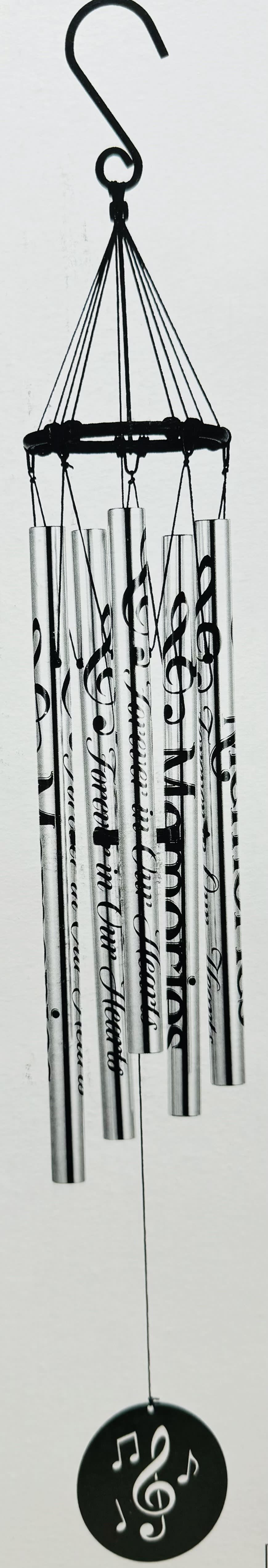 " Memories Forever in our Hearts" Wind Chime - A lyrical stainless steel wind chime engraved with the words "Memories" and "Forever in Our Hearts" offers a calm, reflective presence for sympathy and funeral settings or as a year-round memorial keepsake. The tall mixed-color/monochrome palette-silver tubes with flowing black script and musical notes-creates a soothing visual and audible tribute that helps the person you're honoring feel remembered and cherished.  Hand-tuned metal tubes hang from a black circular frame and finish with a round black windcatcher disc pierced with musical symbols and a treble clef, reinforcing the musical theme. The piece measures 37" long from the top of the gathering ring to the bottom of the windcatcher (overall 5" x 37" height) and includes a 2" hook for easy hanging. A matching green metal easel stand with a triangular base is available for presentation if you prefer a freestanding display; choose the deluxe option to include the stand.
