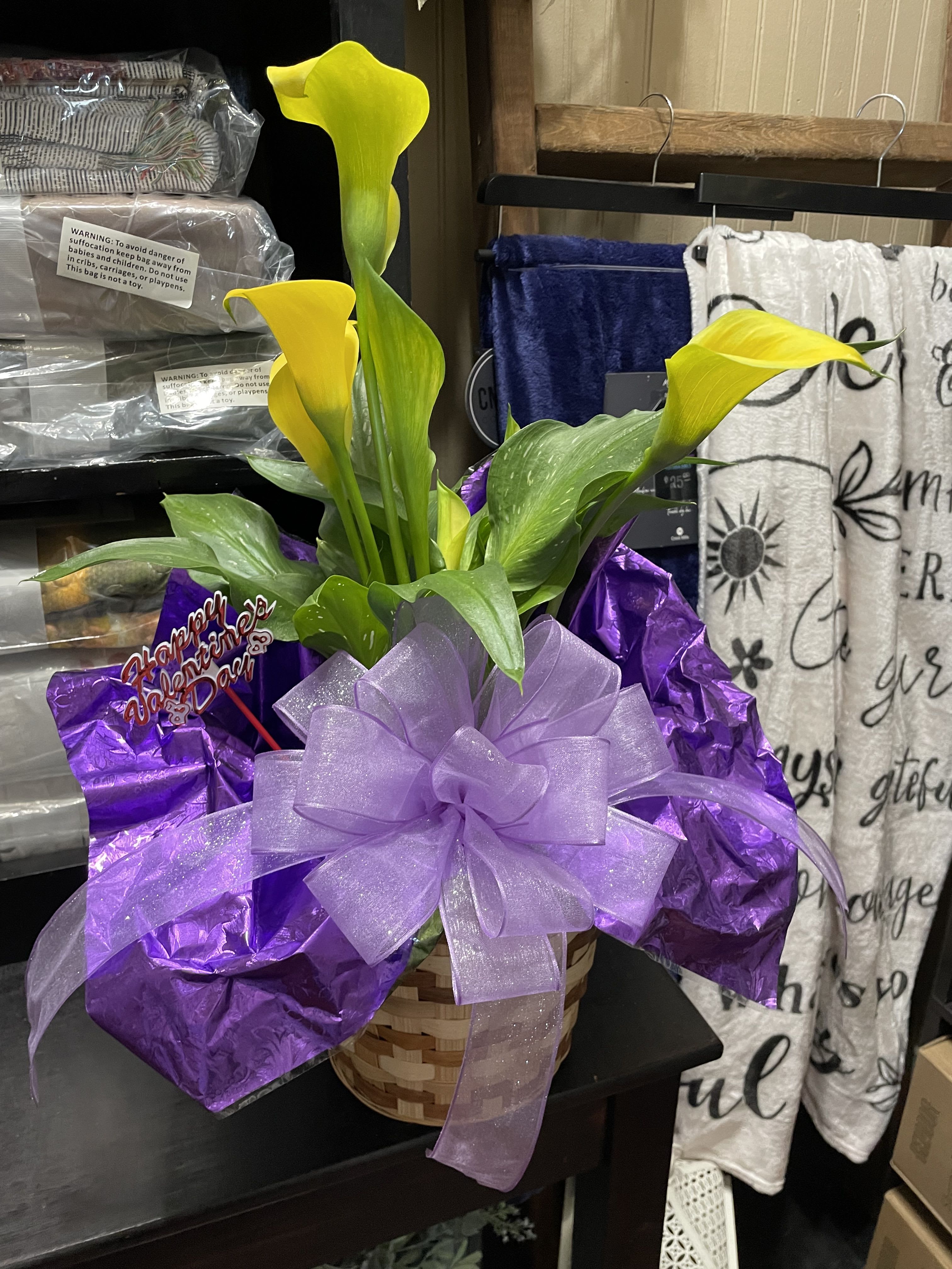 Yellow calla lilies in a basket wrapped with purple ribbon
