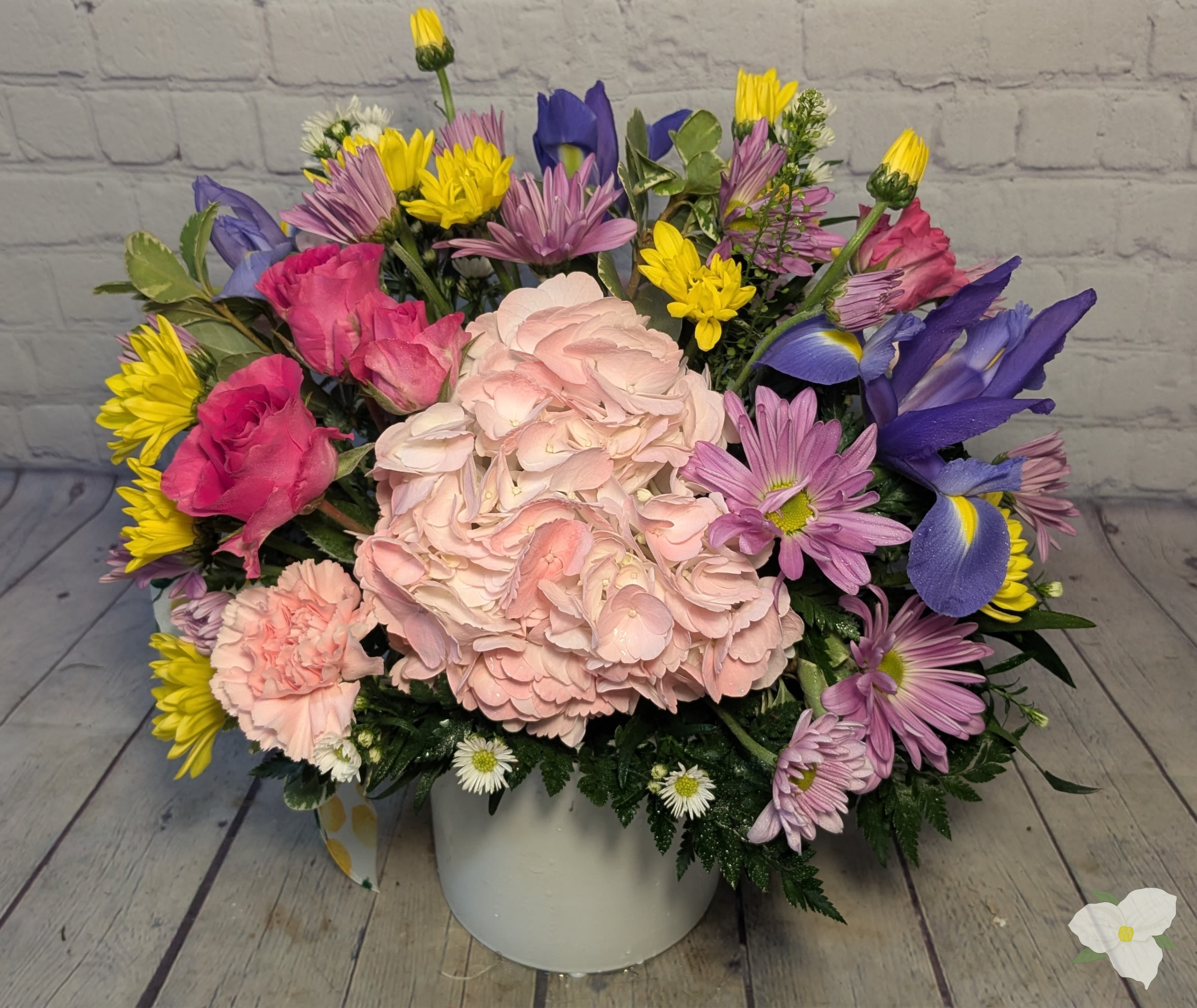 Mixed bouquet of pink, purple, yellow, and white flowers in a white vase