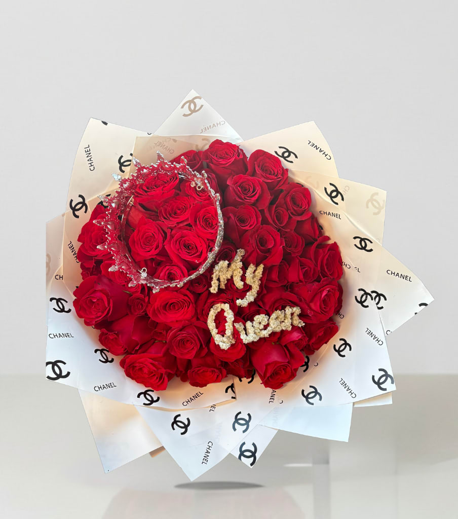 Red rose bouquet wrapped in Chanel-logo paper with a jeweled crown