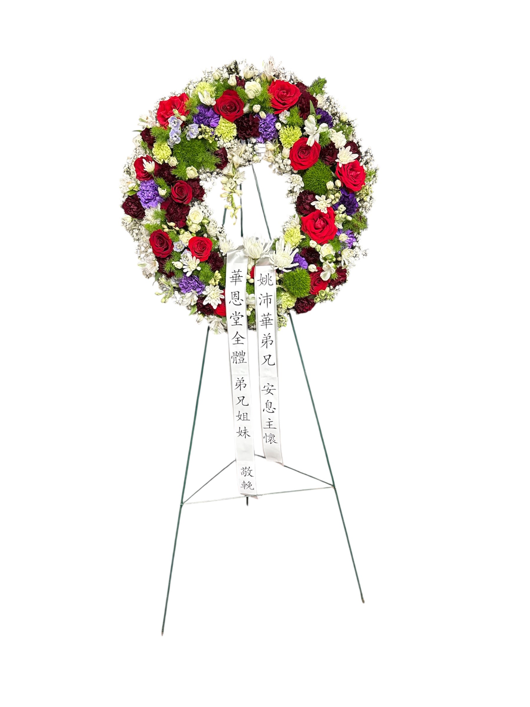 Circular funeral wreath of red, white, purple, and green flowers on a stand
