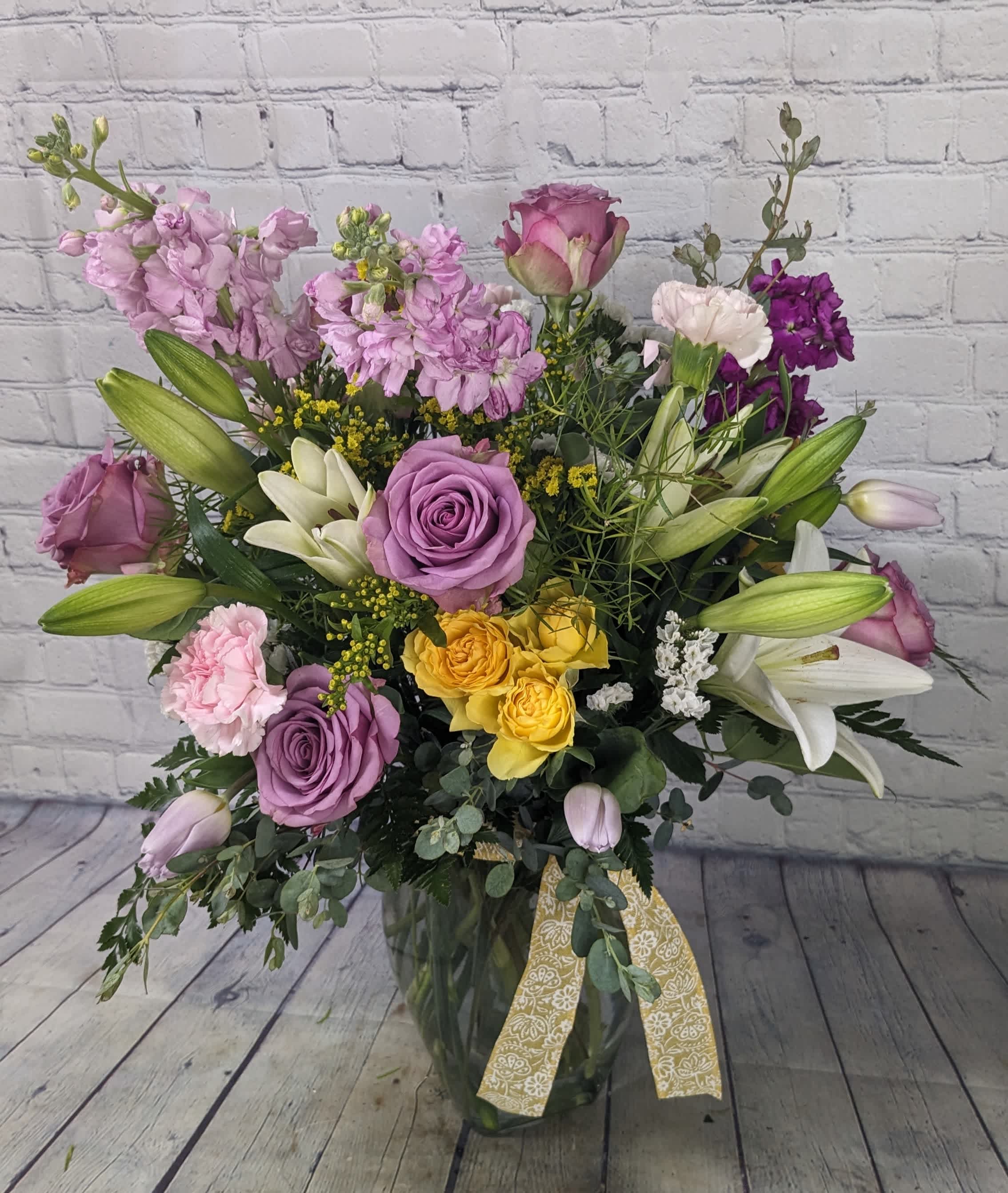 Mixed bouquet of roses, lilies, and purple blooms in a glass vase