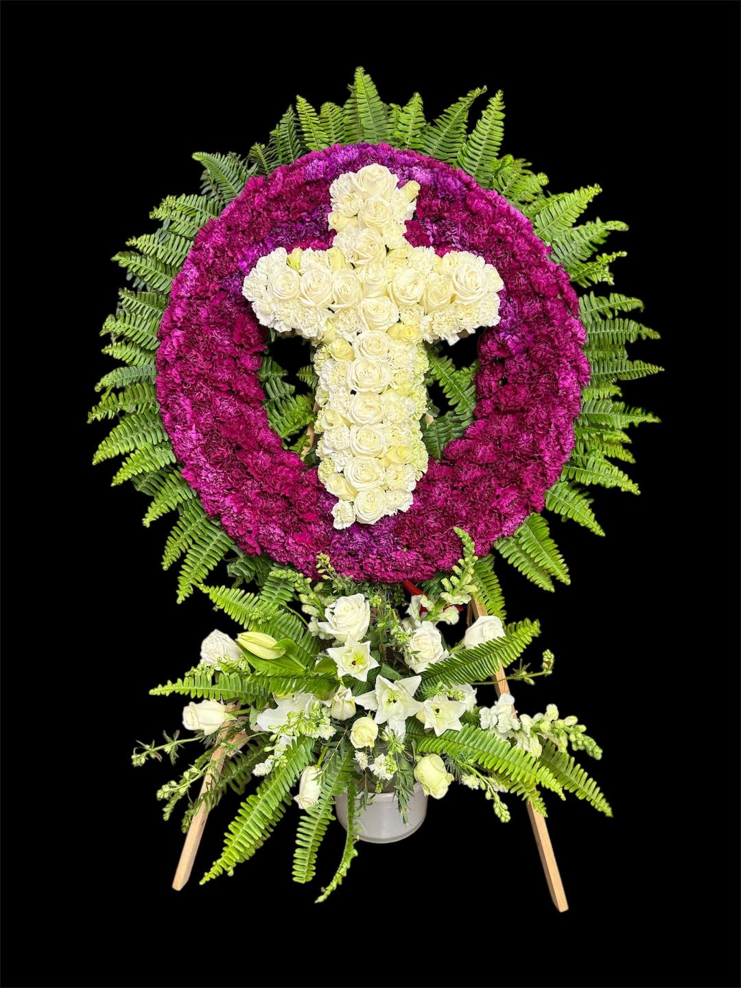 Floral standing tribute with a white cross in a magenta wreath