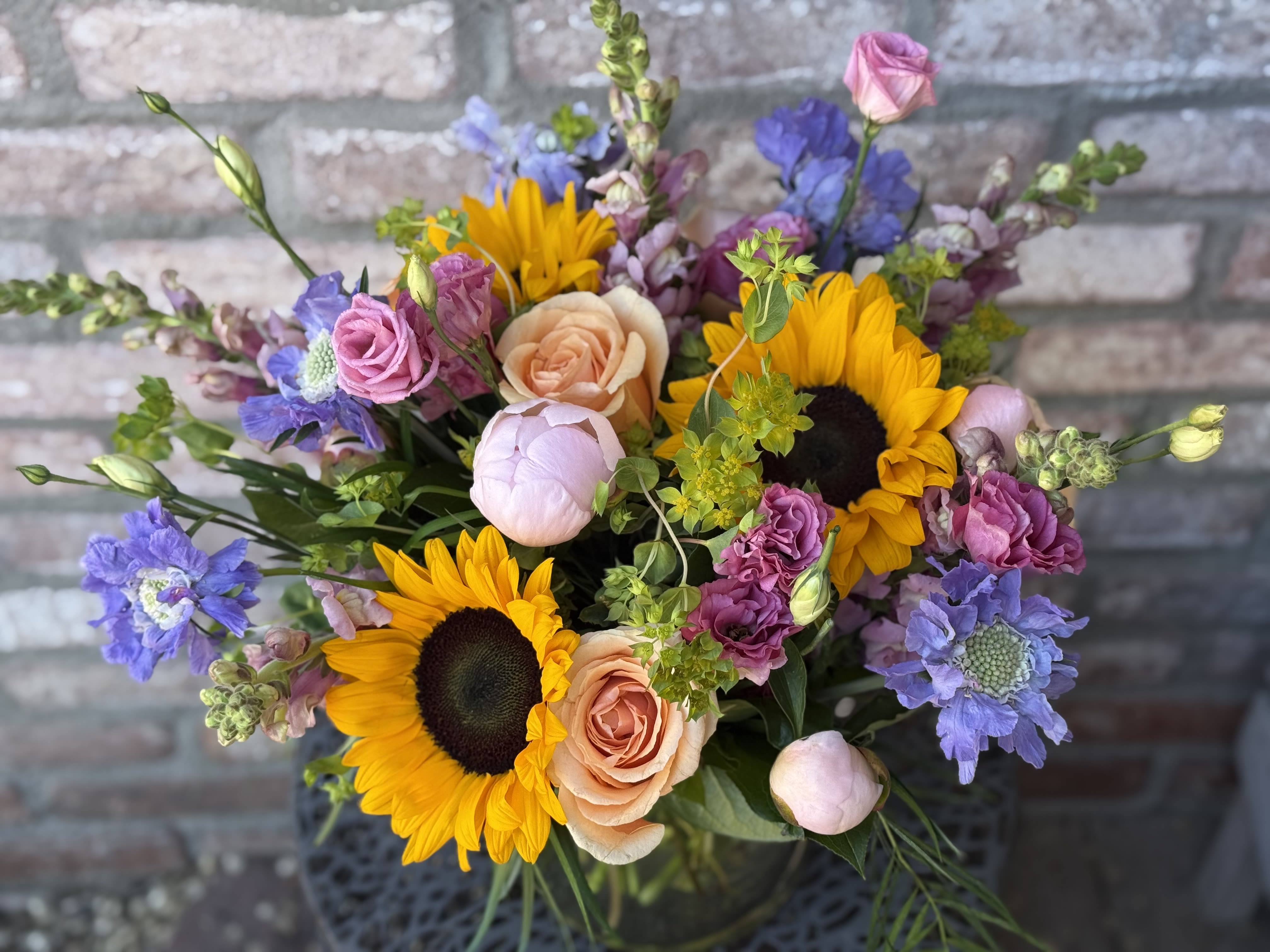 Mixed bouquet with sunflowers, peach roses, and purple blooms in a vase