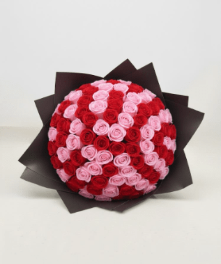 Round bouquet of red and pink roses wrapped in dark paper