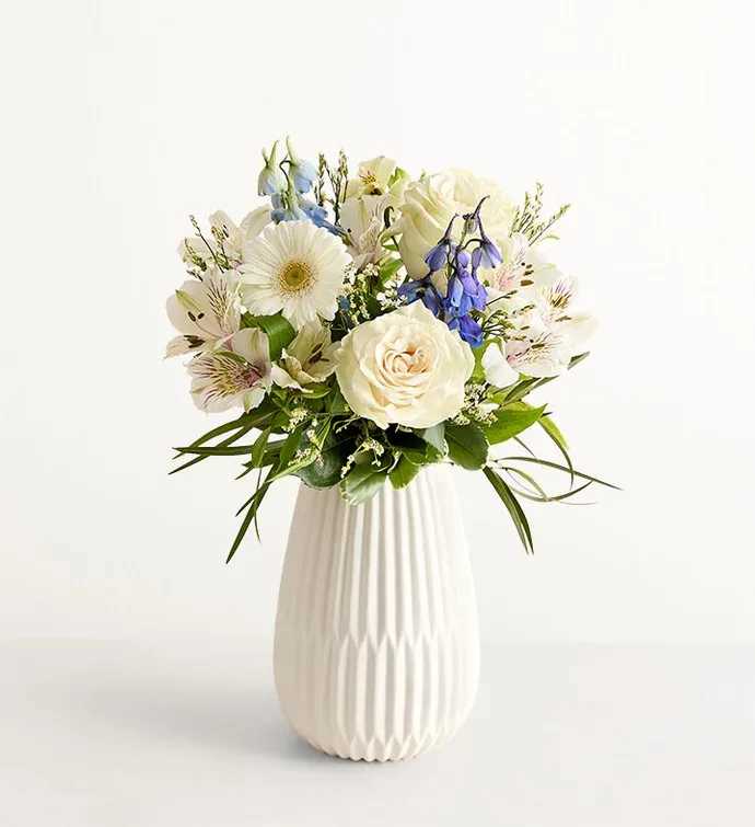 Treasured Memories Blue &amp; White - Soft white roses mingle with pale alstroemeria and cool blue delphinium to create a serene flower arrangement perfect for a birthday bouquet, spring celebration, or a thoughtful thank-you. The Treasured Memories Blue &amp; White arrangement reads calm and modern - the taller blue spikes rise above the rounded white blooms so the recipient will instantly feel noticed and comforted by the fresh, airy palette.