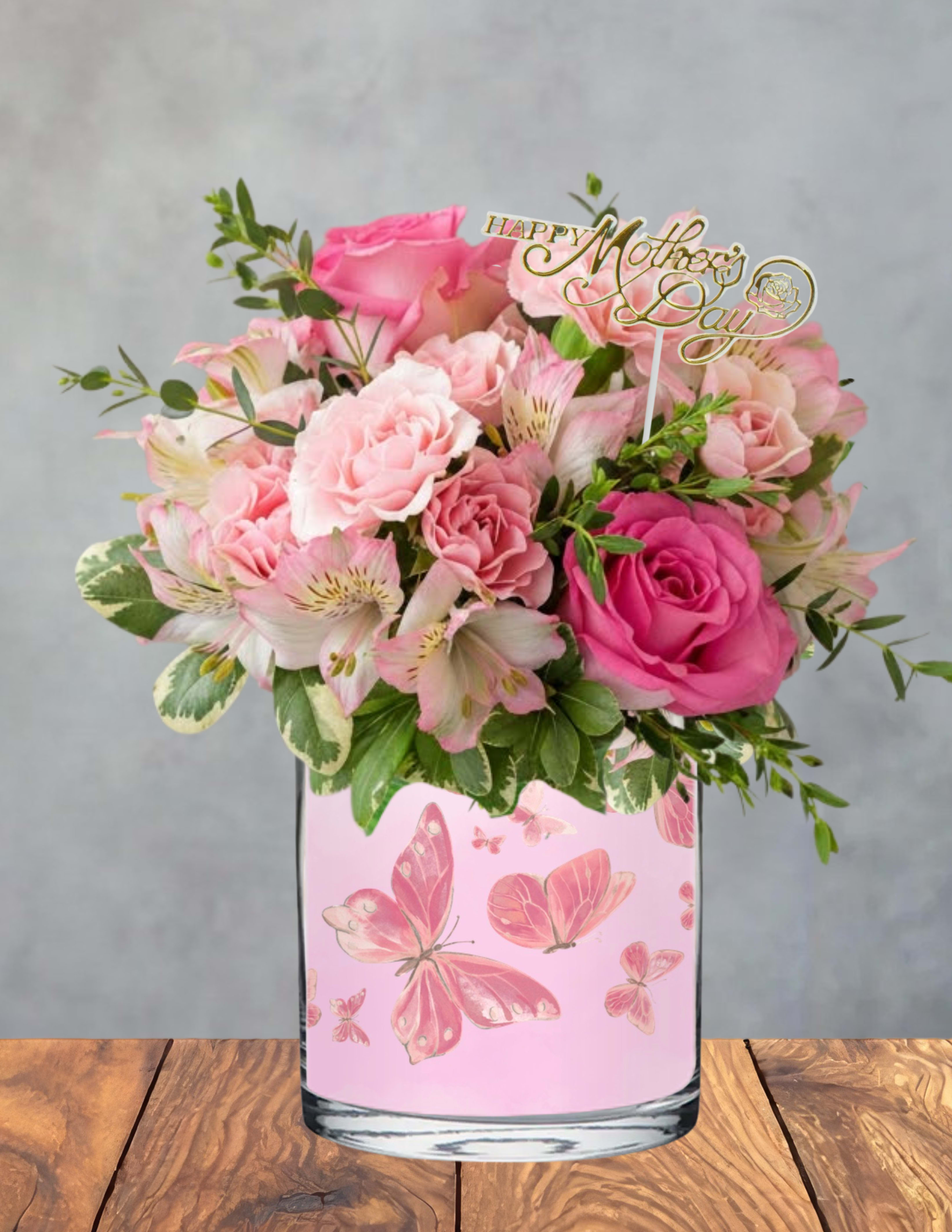 Butterfly garden  - A cluster of pink roses in varied shades creates an immediate, joyful impact-perfect for a Mother's Day bouquet that reads as affectionate and feminine the moment she sees it. This Butterfly garden arrangement is a Mother's Day bouquet designed to make the person you're thinking of feel cherished: soft pink roses paired with pale alstroemeria and fresh greenery give a warm, uplifting impression that says "thank you" and "I love you" without words.  The flowers are arranged in a clear glass vase wrapped with a delicate pink butterfly design, giving the whole gift a polished, whimsical look. Pale alstroemeria add texture and light contrast to the fuller rose heads, while small sprigs of greenery bring a fresh, gardenlike feel. A gold "Happy Mother's Day" topper is included to make the occasion unmistakable and gift-ready.  This arrangement suits moms, grandmothers, or any maternal figure who delights in classic blooms with a feminine touch-ideal for brunches, deliveries, or bedside surprise moments. Vase-arranged and finished with the topper, it arrives ready to display; to keep flowers looking their best, refresh the water every couple days and trim stems slightly when you change the water.