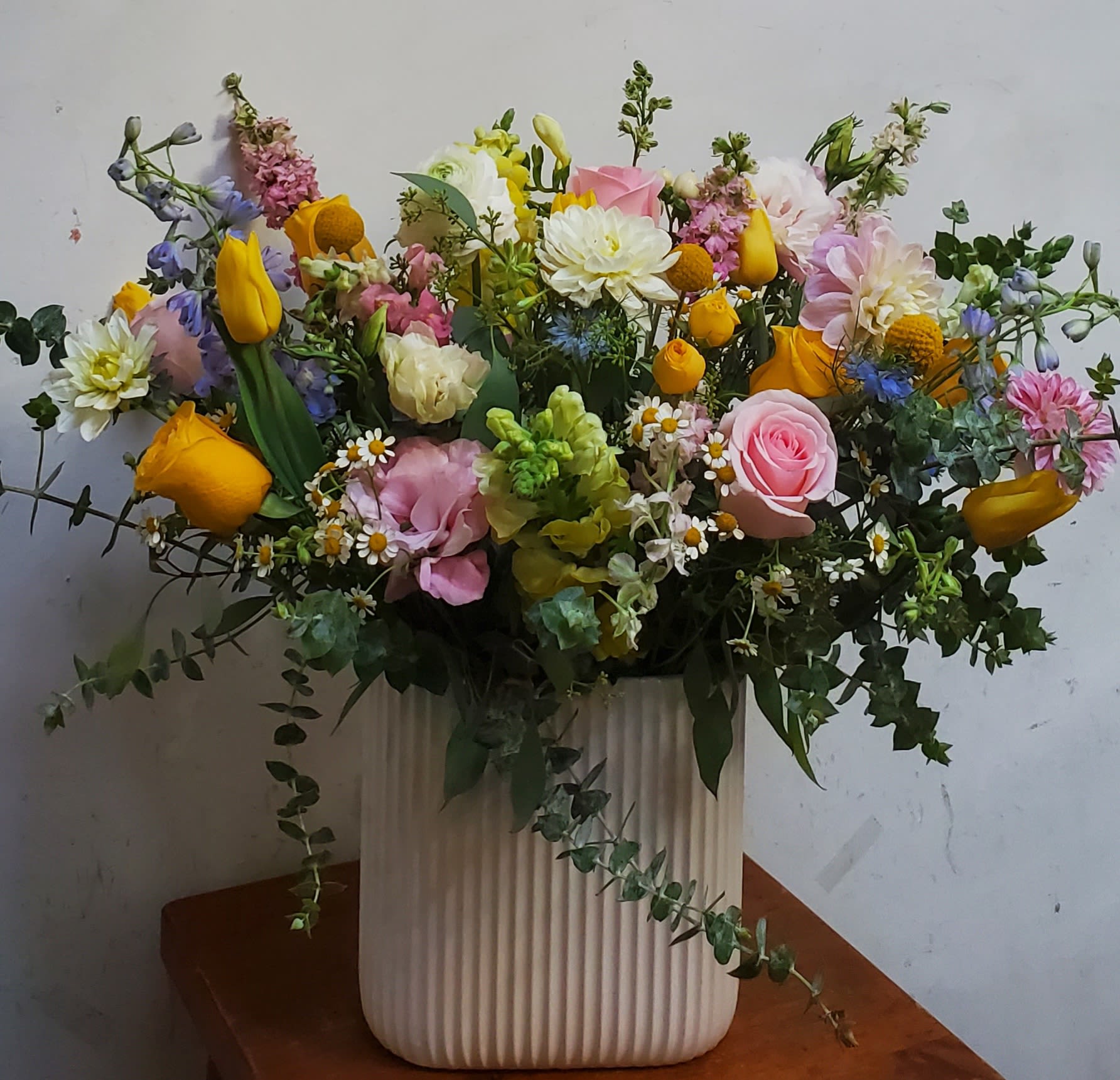 Mixed bouquet in a ribbed white vase with pink, yellow, and white flowers